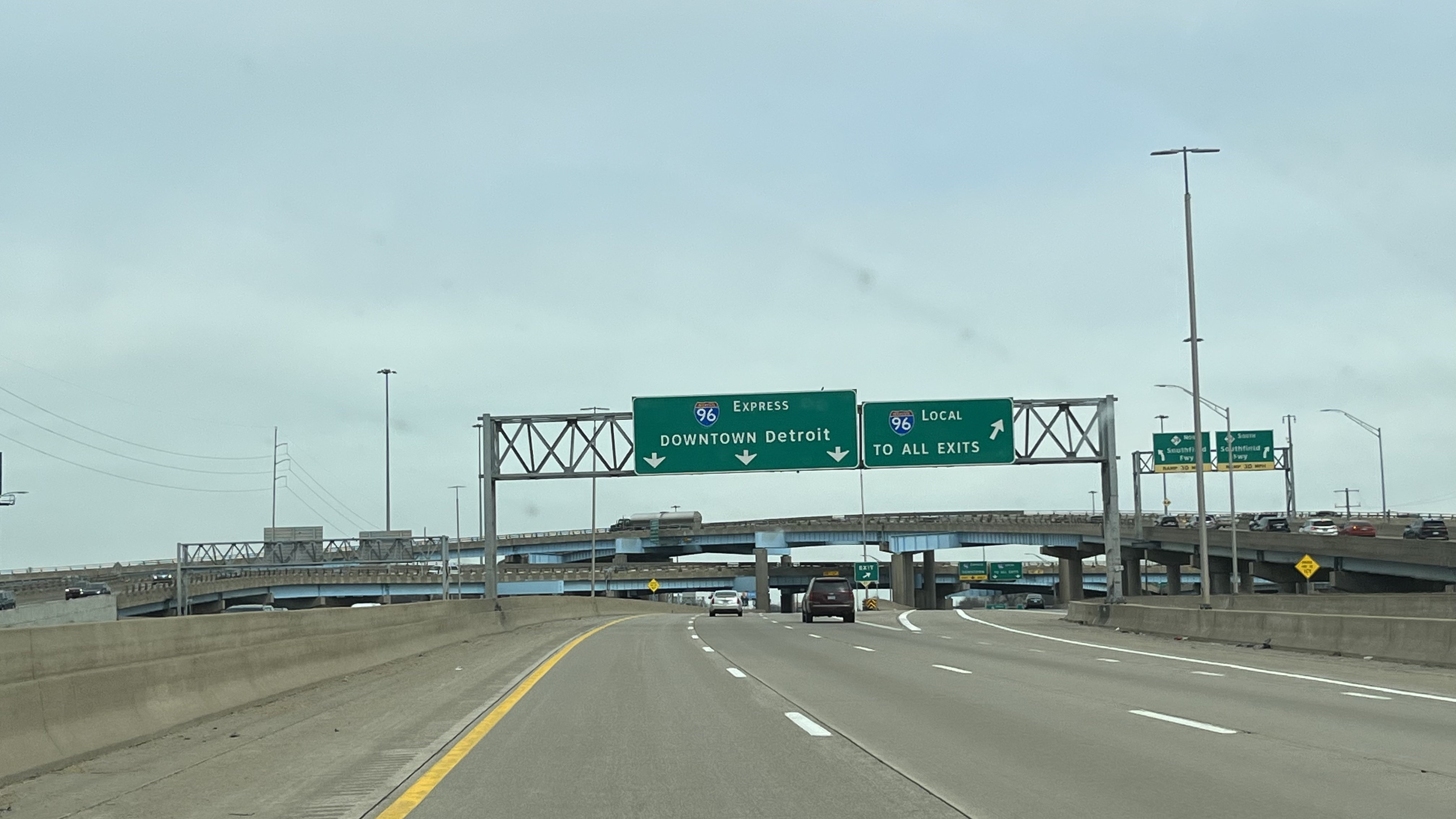 Multi-lane freeway with green overhead signs for express and local lanes.