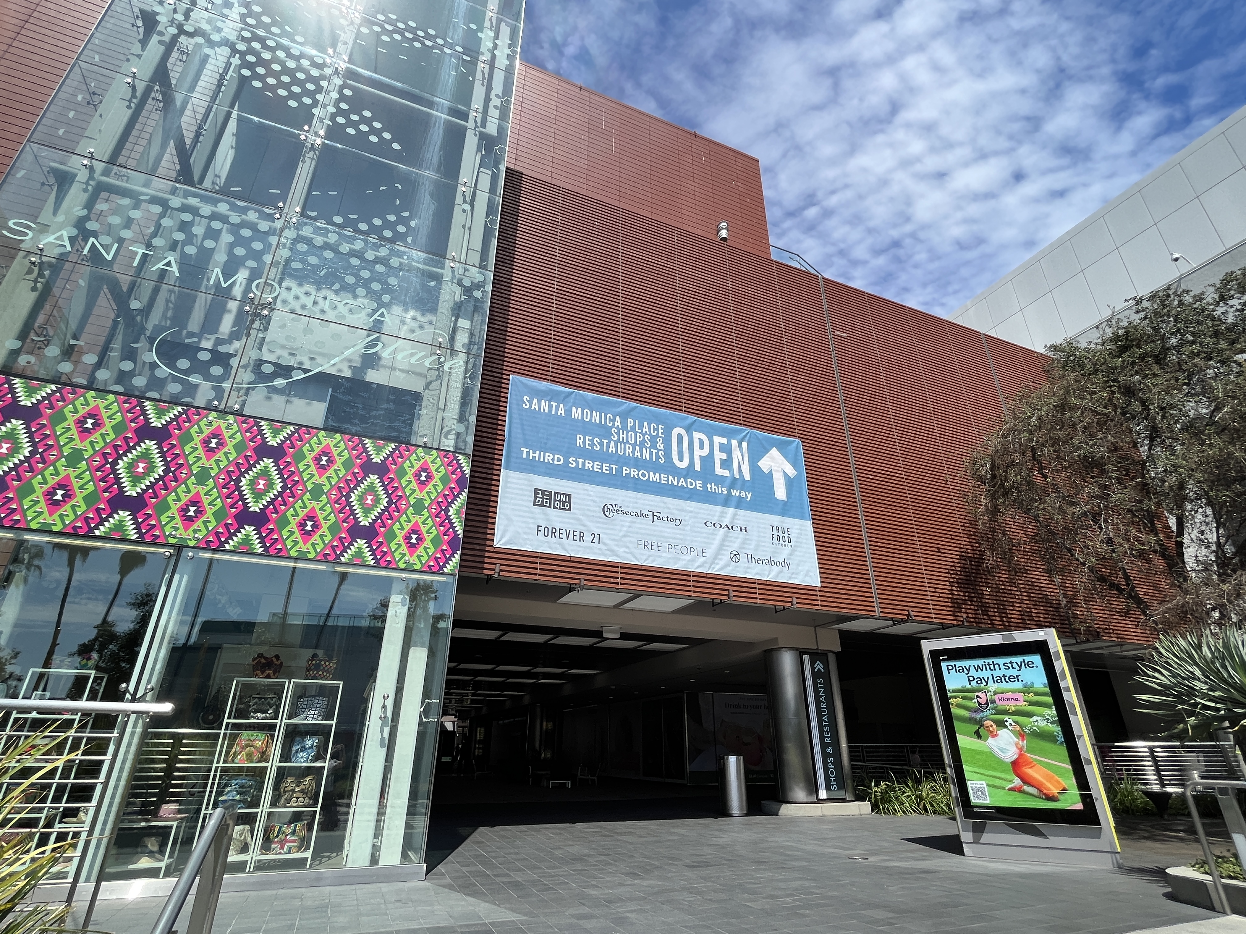 Exterior facade of a shopping mall with storefronts and an open banner at street level.