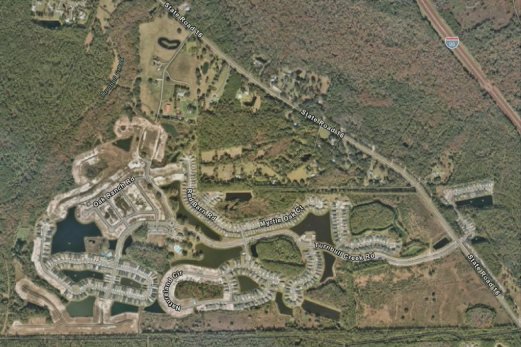 Aerial satellite view of a residential development with curved streets, finished homes, and empty lots.