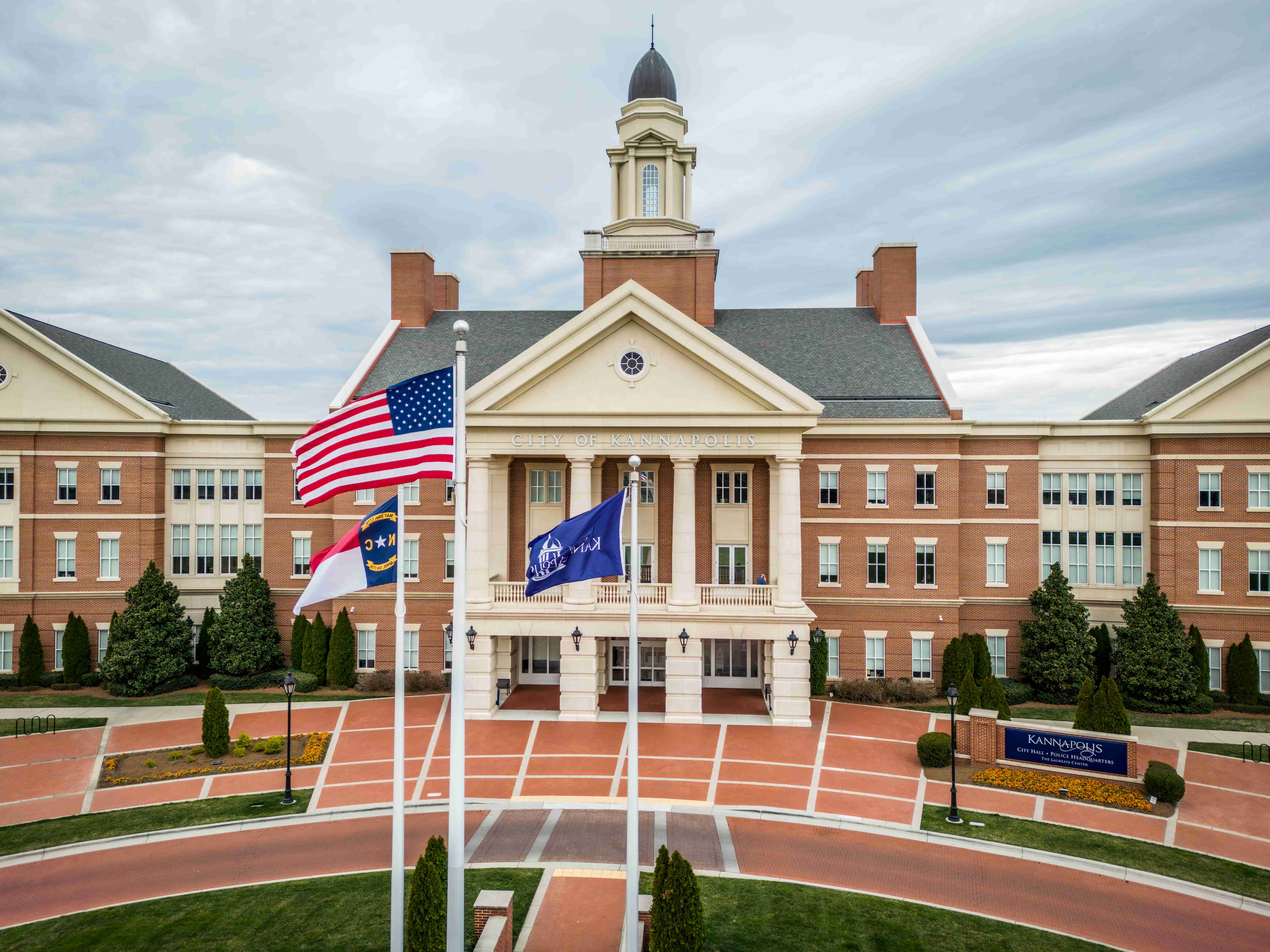 Brick colonial-style government building with a white cupola and three flagpoles out front.