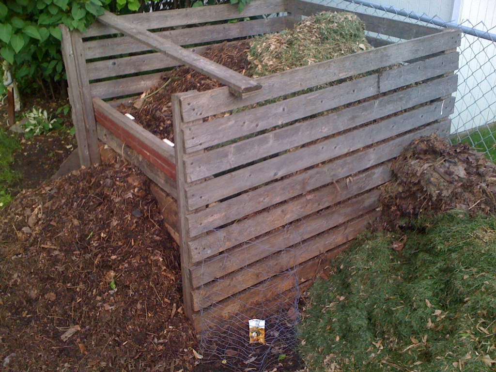 A wooden compost bin filled with decomposing organic material in a backyard garden.