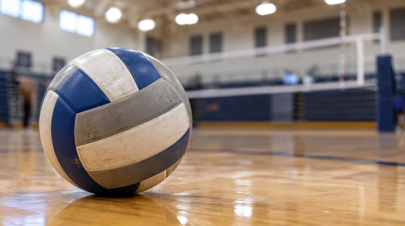 A volleyball sitting on a hardwood gym floor near a net.