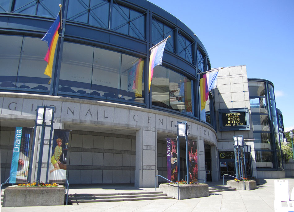Exterior of a performing arts center with curved glass facade and rainbow-colored flags.