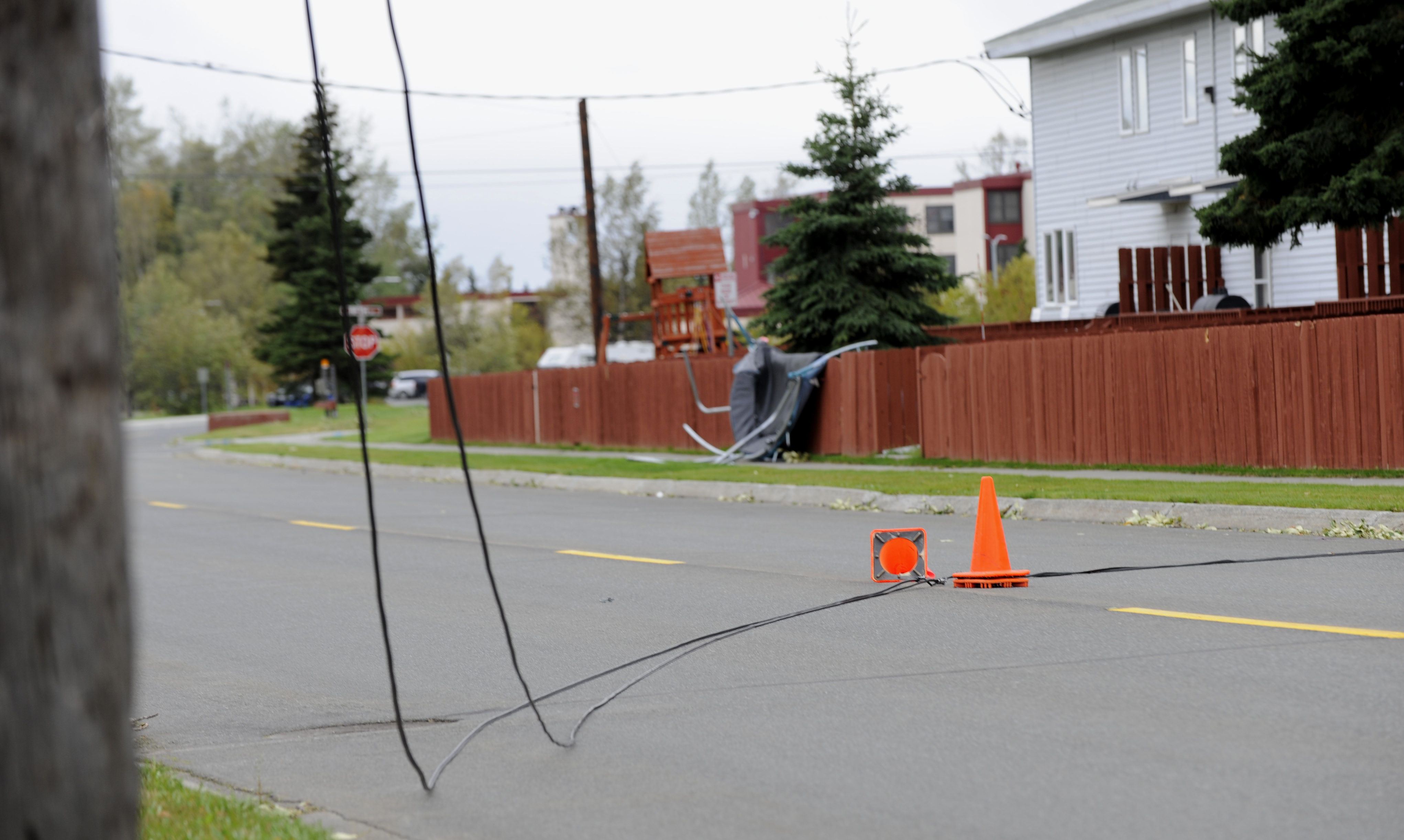 Downed power line on a residential street, marked by two orange traffic cones.