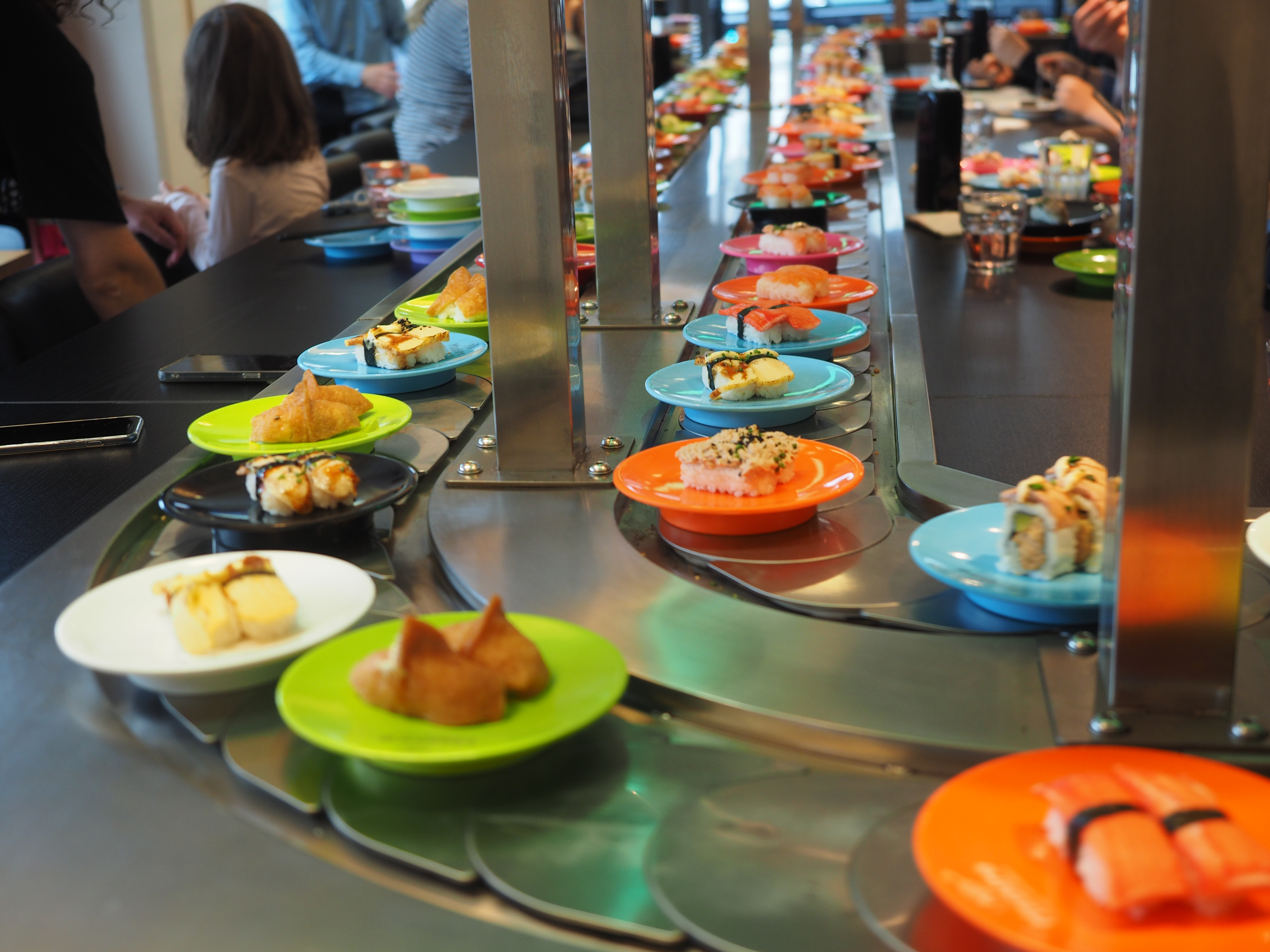 Colorful plates of sushi moving along a stainless steel conveyor belt in a restaurant.
