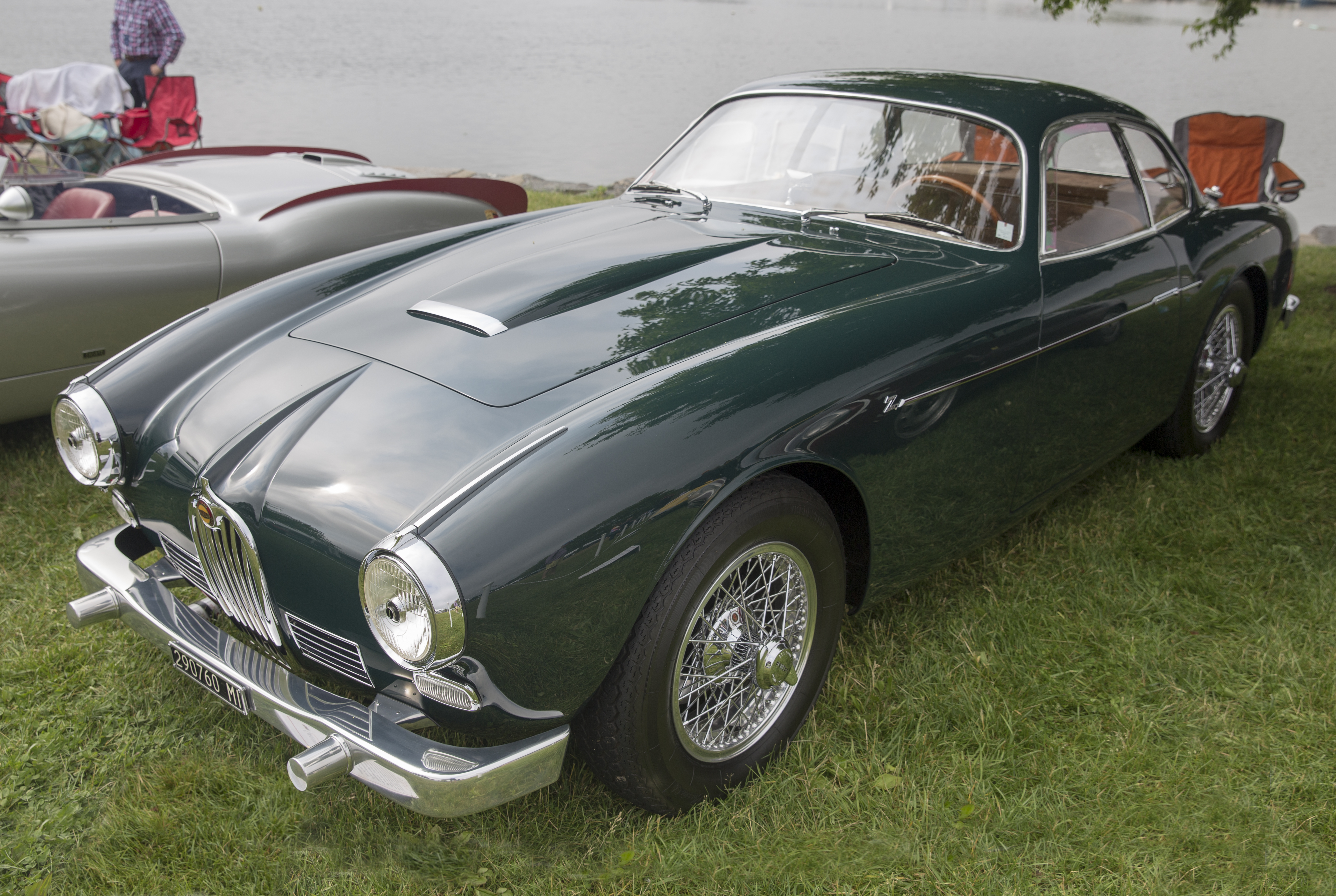 Dark green vintage Jaguar coupe with wire-spoke wheels displayed on a grass lawn.