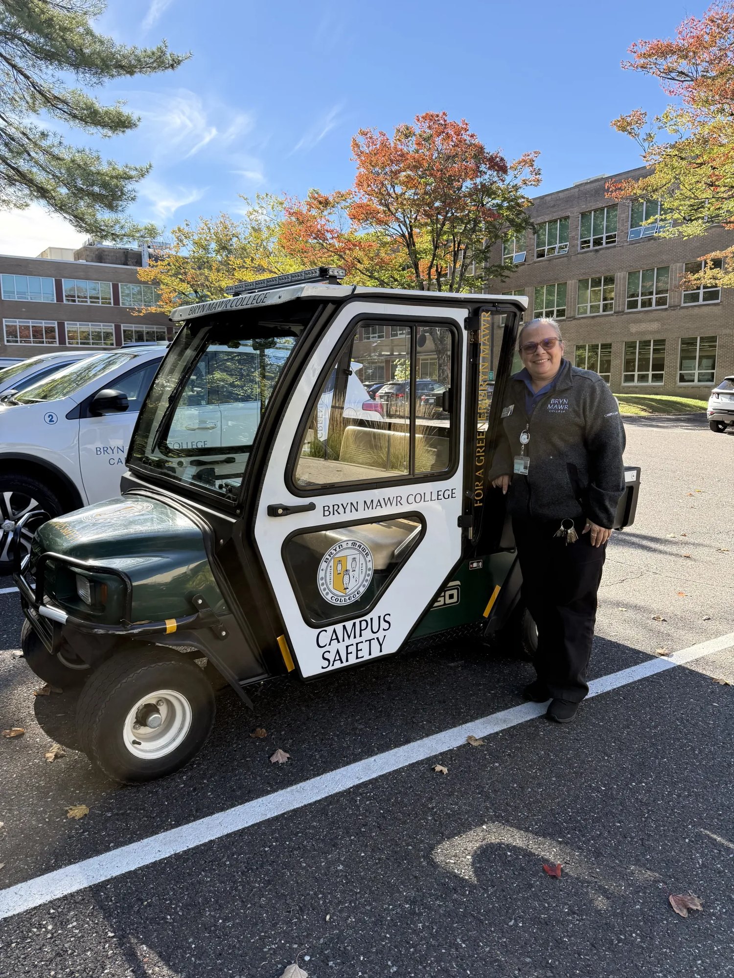 A person in uniform stands beside a green and white electric golf cart in a parking lot.