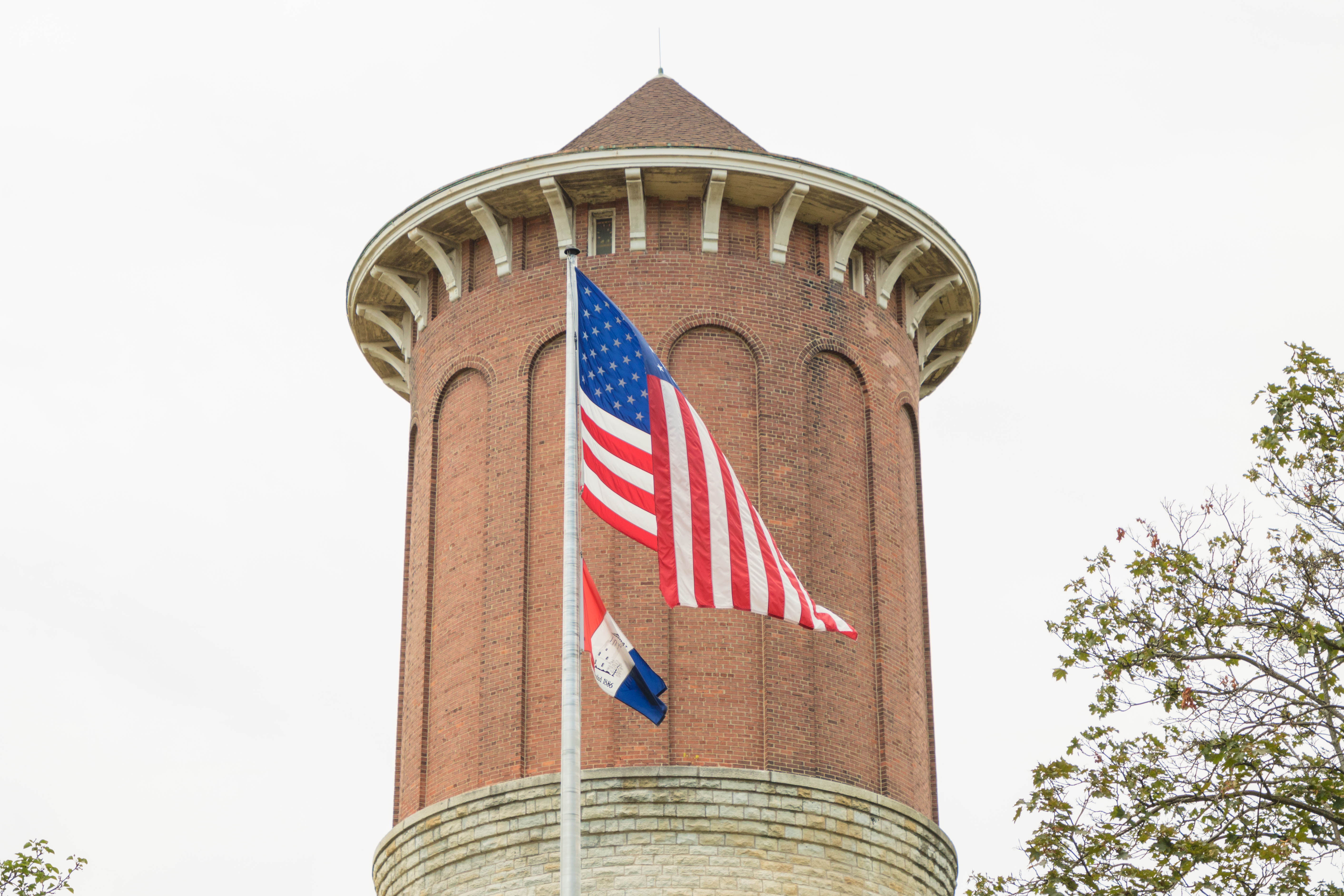 Tall cylindrical brick water tower with conical roof and flags on a pole.