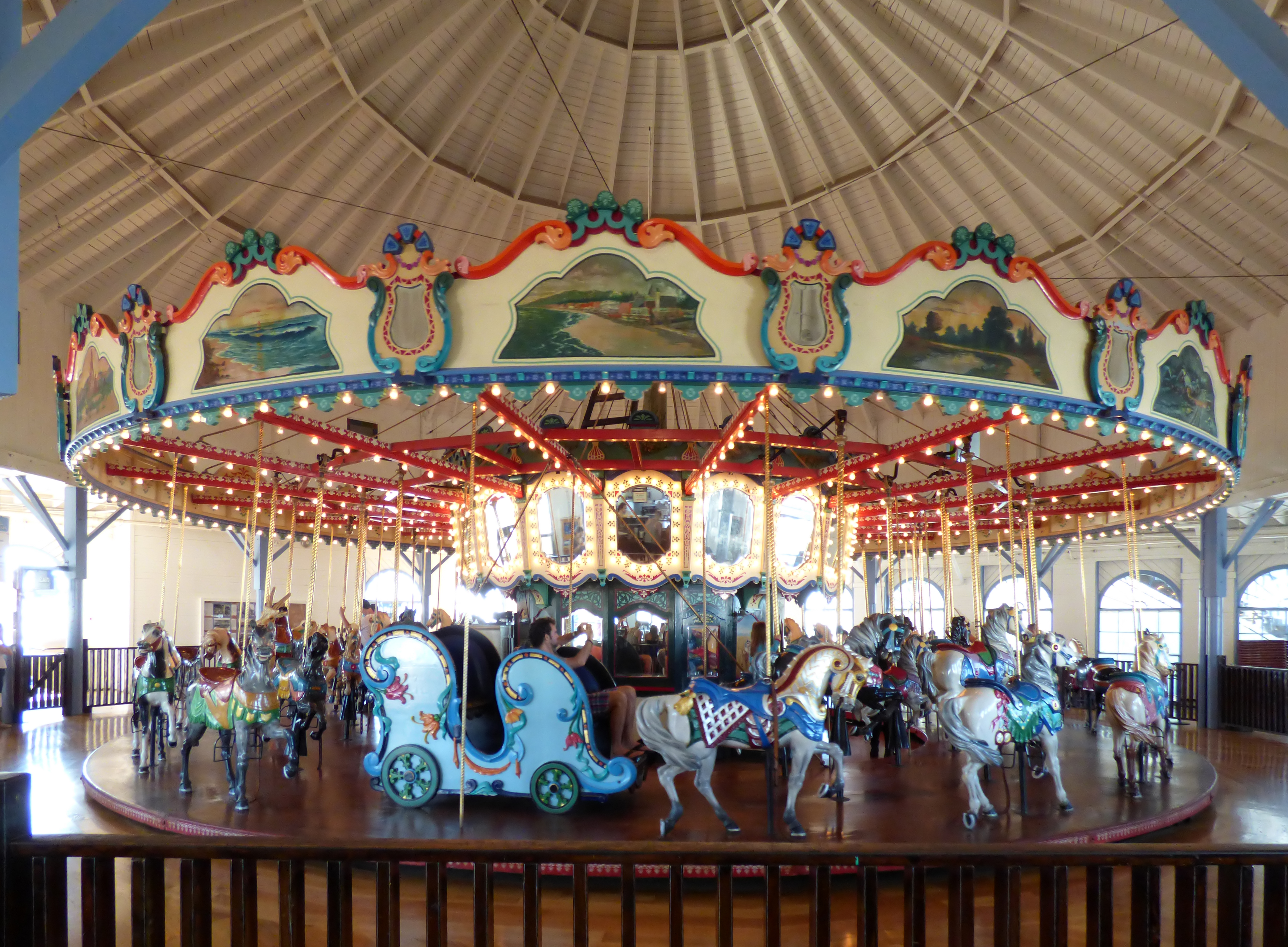 Ornate indoor carousel with painted horses under a domed wooden ceiling.