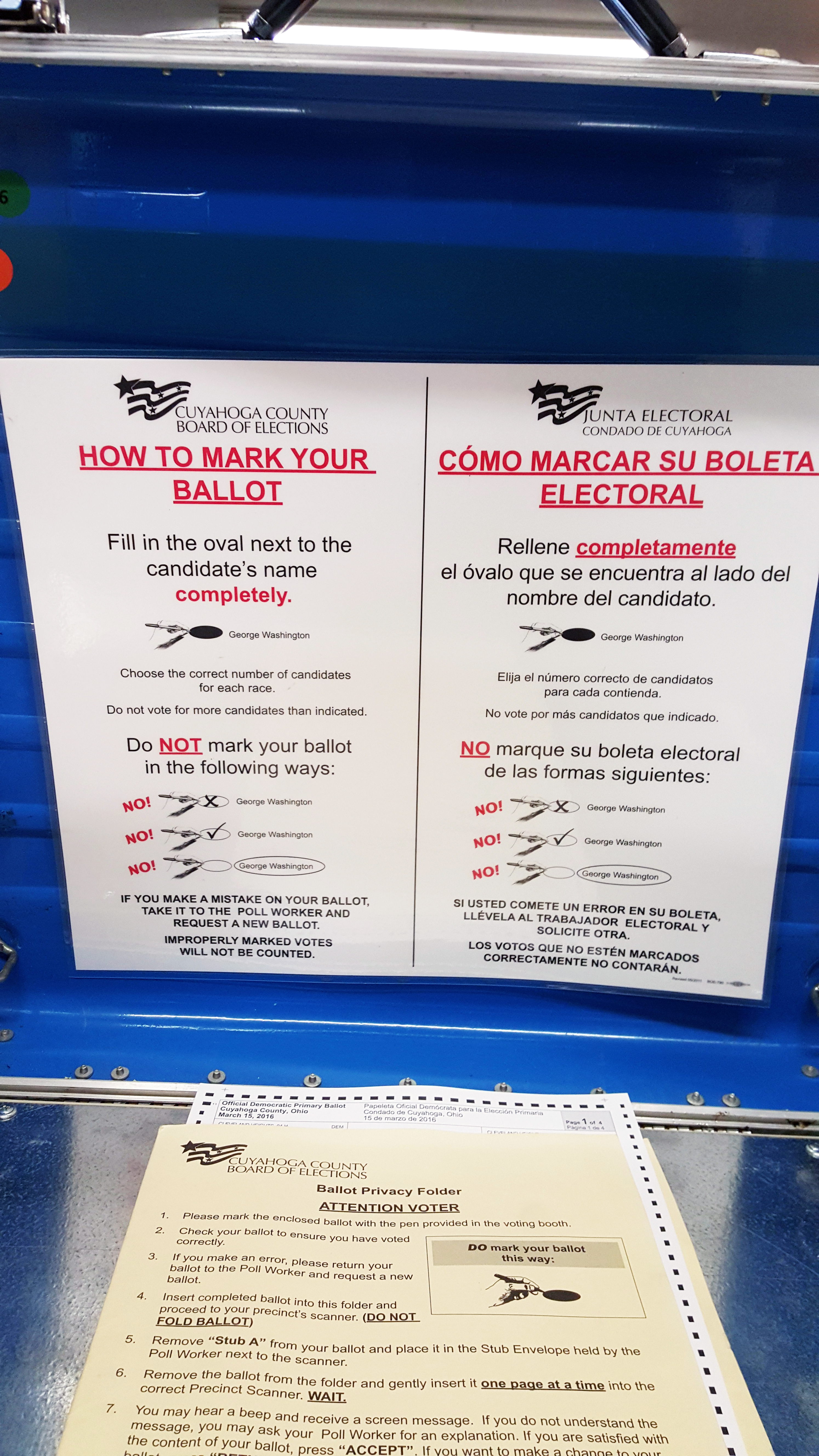 Inside an Ohio voting booth showing an unvoted ballot and bilingual instructions posted on the booth.