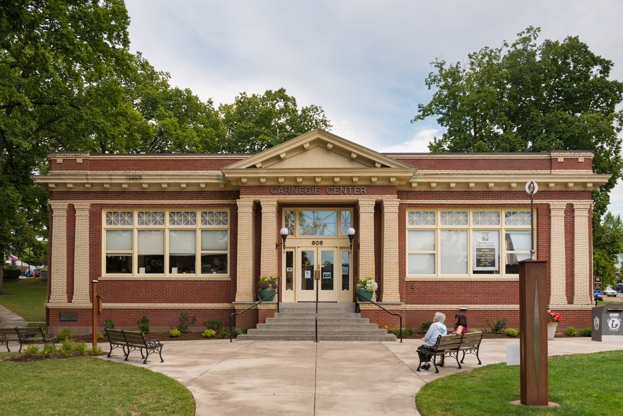 Neoclassical red-brick library building with columns, steps, and a bench on the grounds.