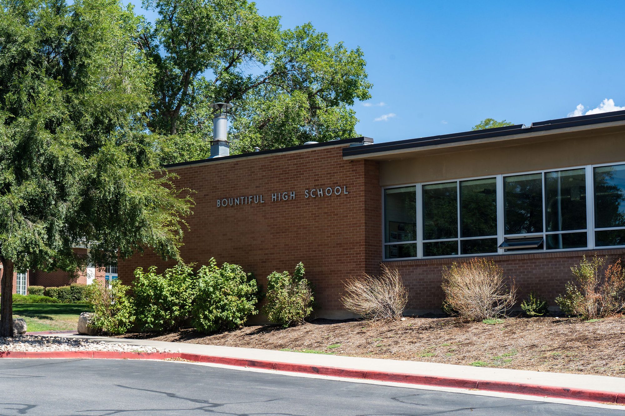 Exterior of a single-story brick high school building with landscaping under a blue sky.