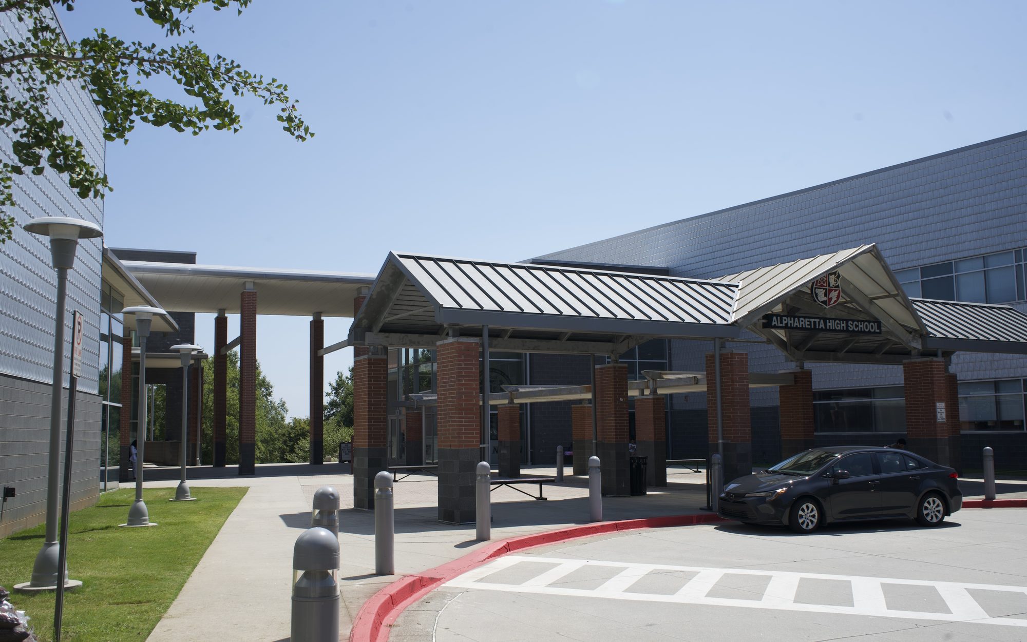 Exterior entrance of a high school with covered drop-off canopy and parked car under blue sky
