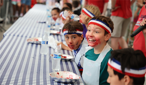 Children with pie-filling-smeared faces grin at a long checkered-tablecloth table.