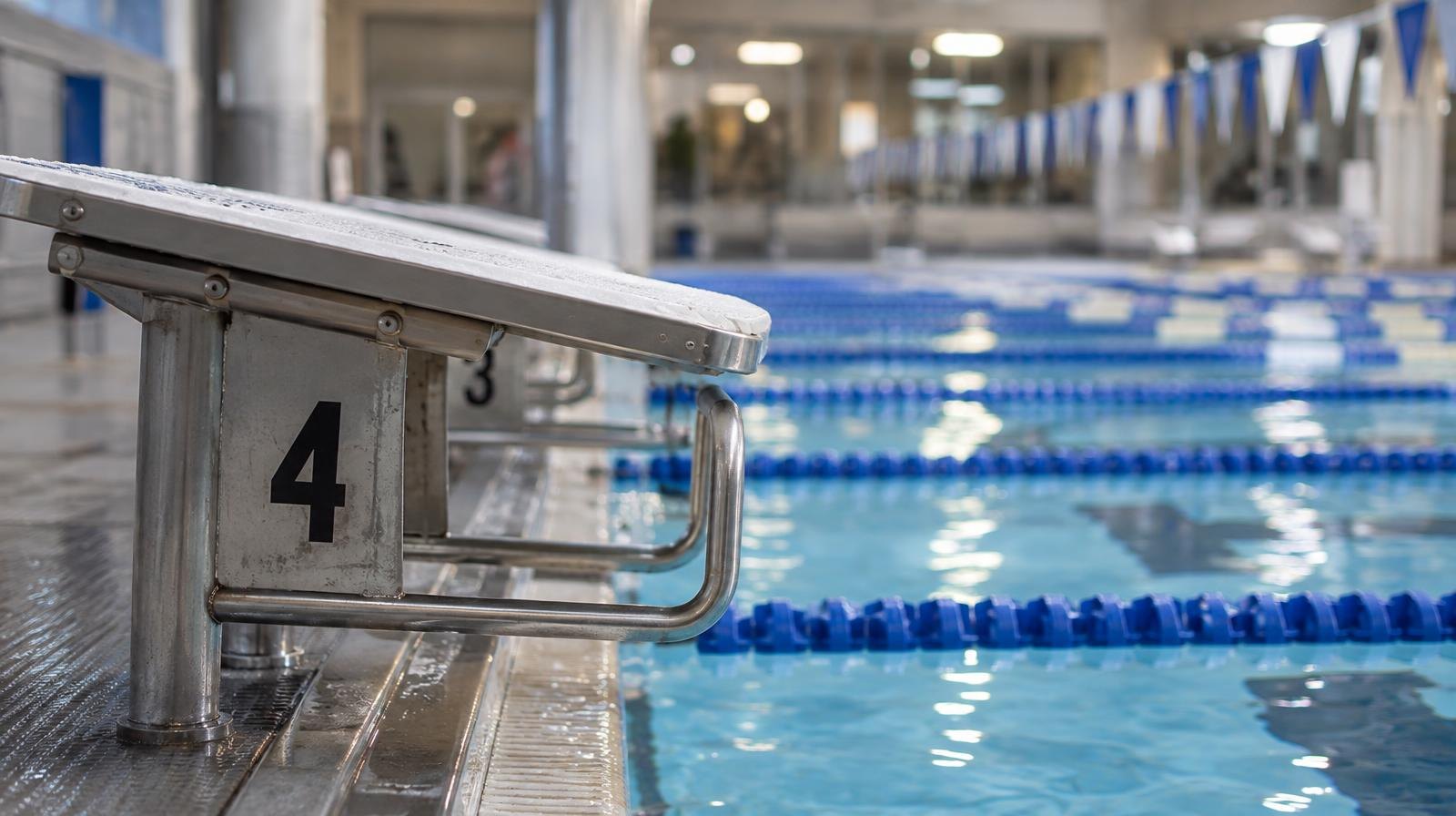 Indoor swimming pool with blue lane dividers and starting blocks viewed from pool deck level.