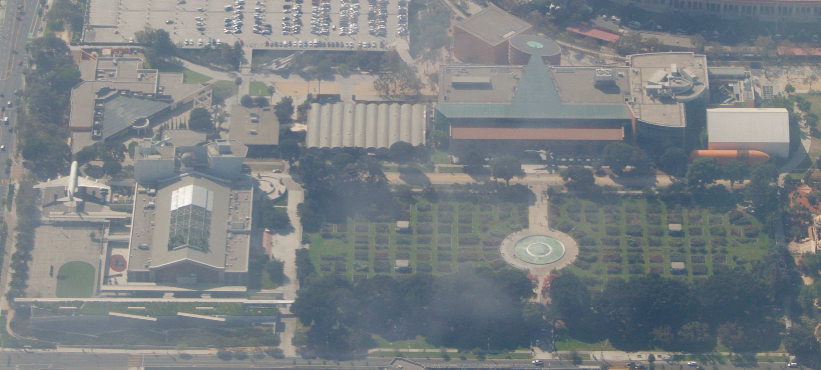 Aerial view of a large urban park with museum buildings, a circular garden, and aerospace exhibits.