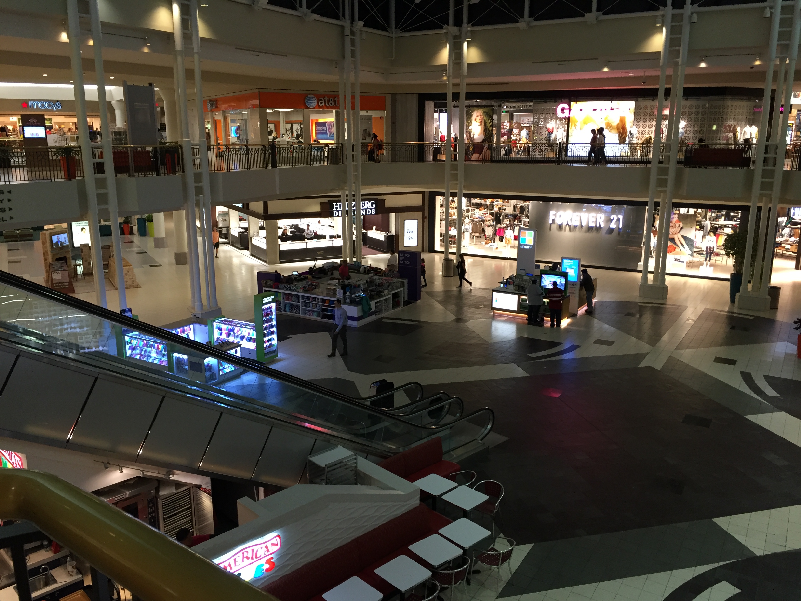 Two-story shopping mall interior with escalators and retail storefronts.