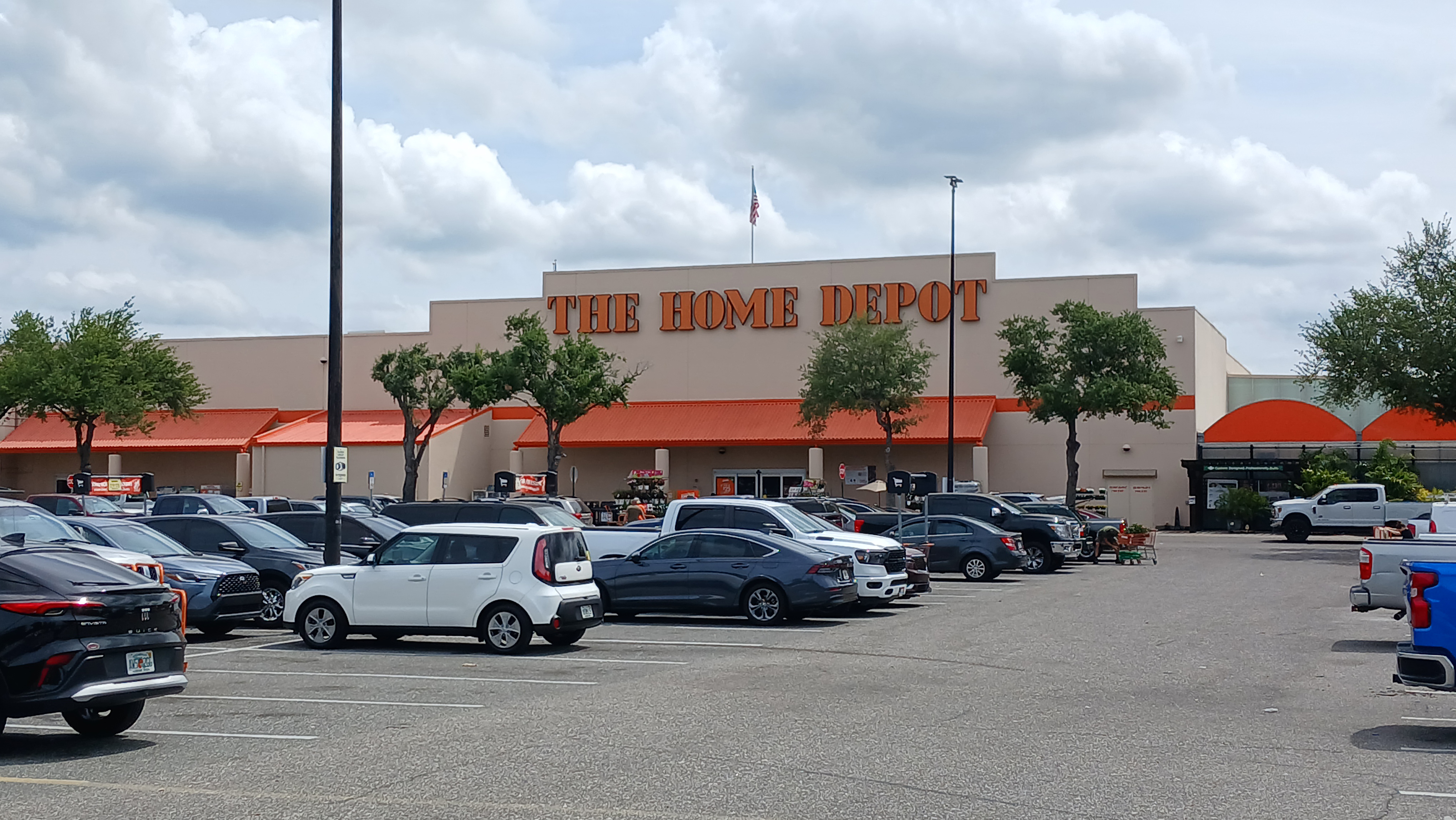 Home Depot store exterior with orange signage and parked cars in front.
