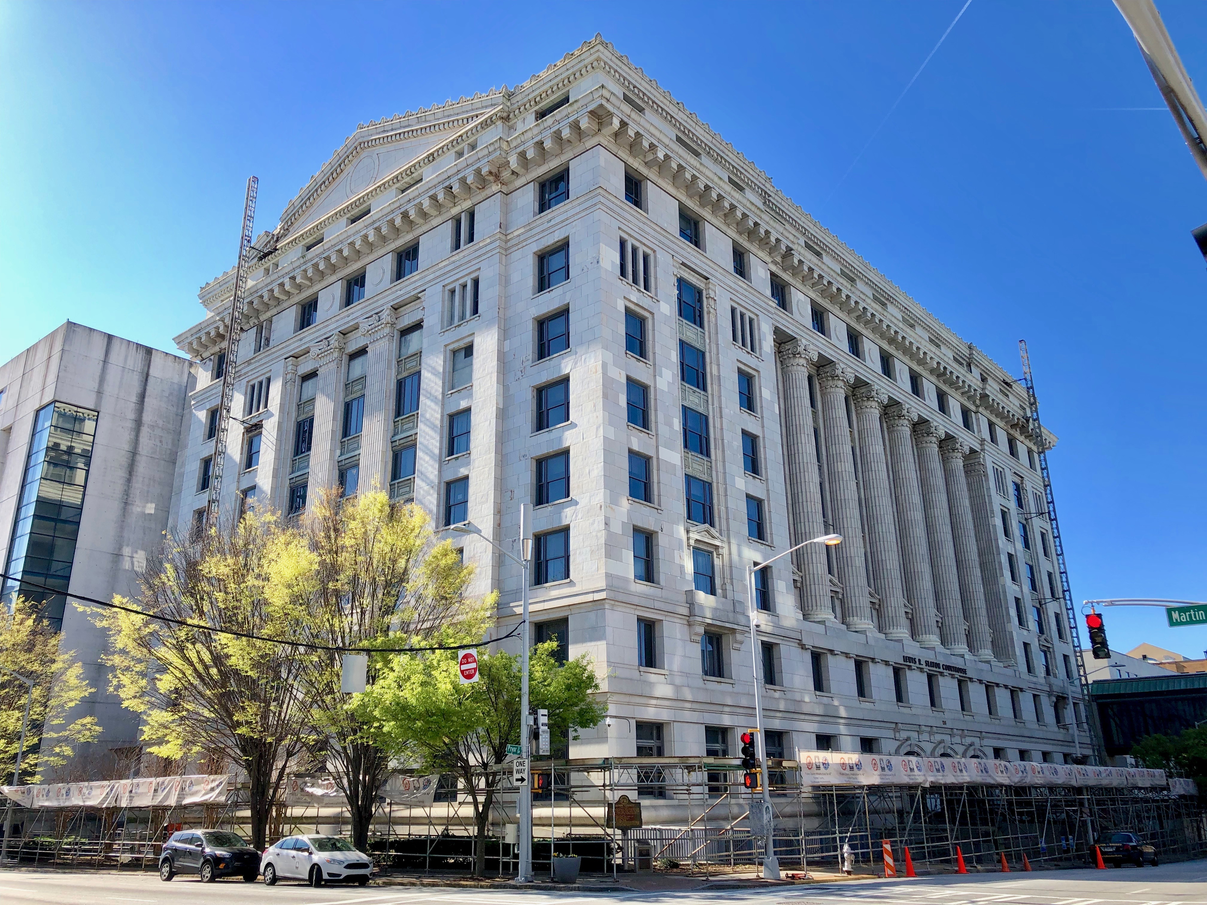 White neoclassical courthouse at a street corner with scaffolding and leafy trees.