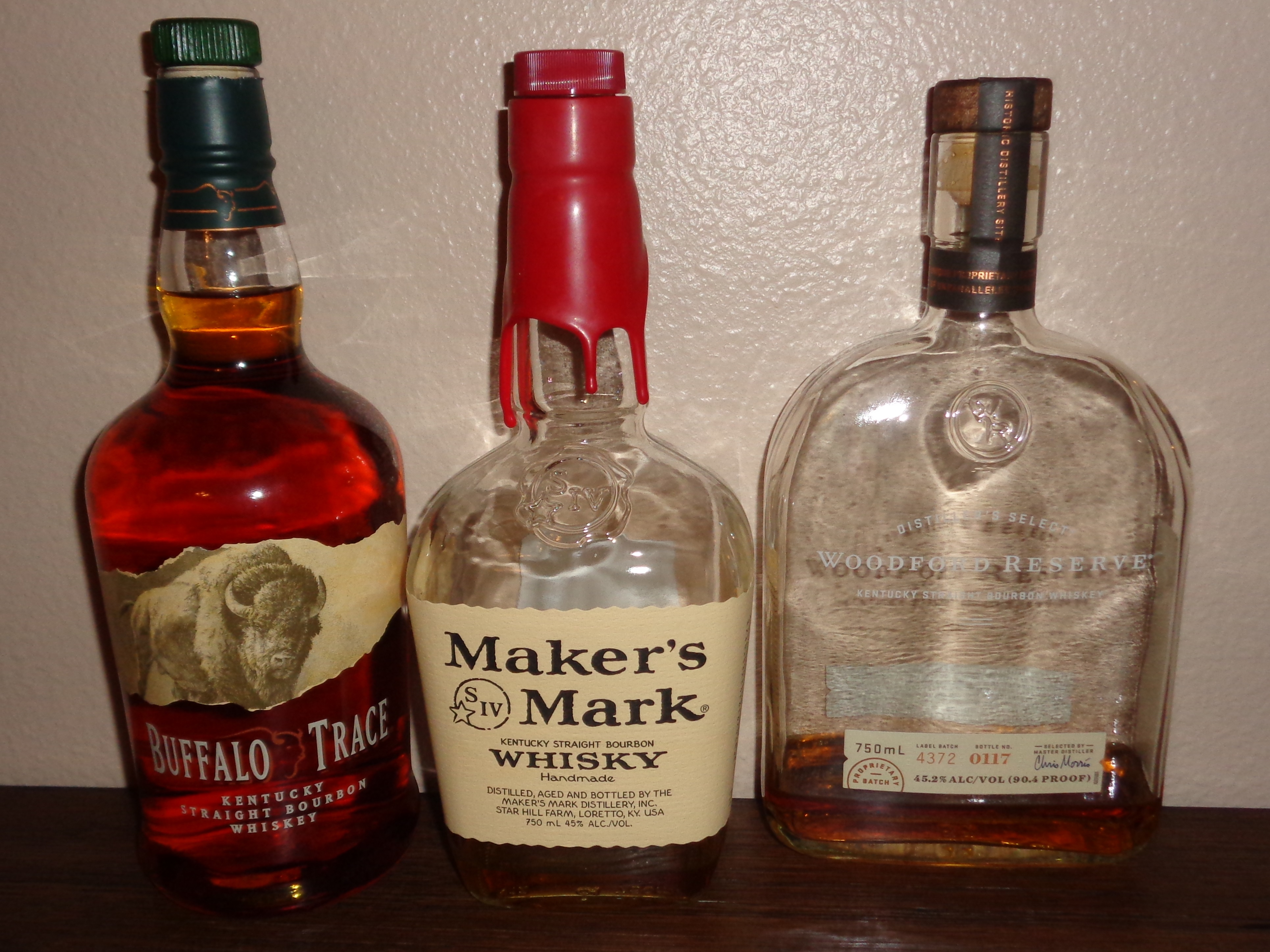 Three Kentucky bourbon whiskey bottles arranged on a wooden surface.