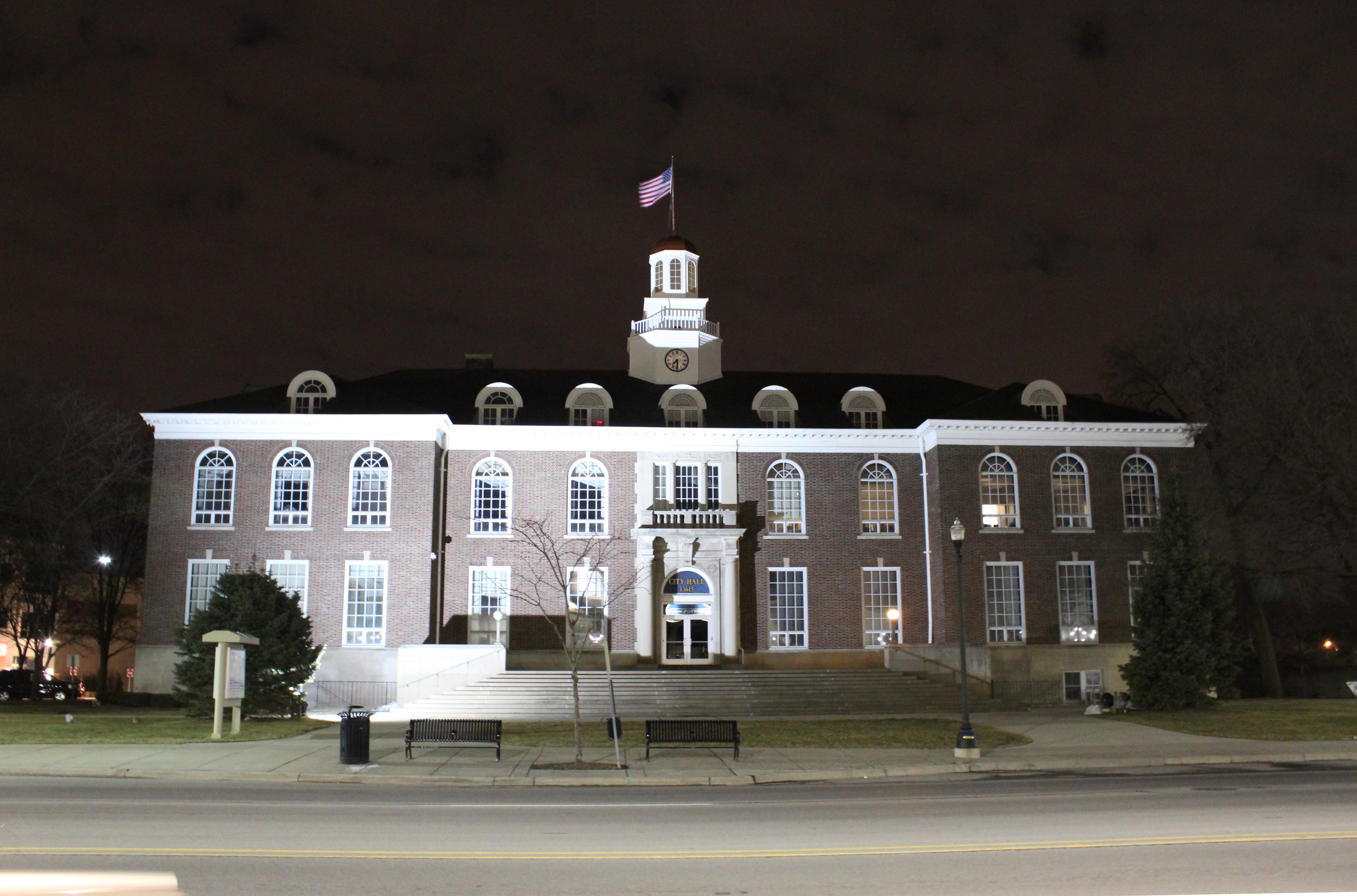 Illuminated red brick city hall building at night with a clock tower and American flag