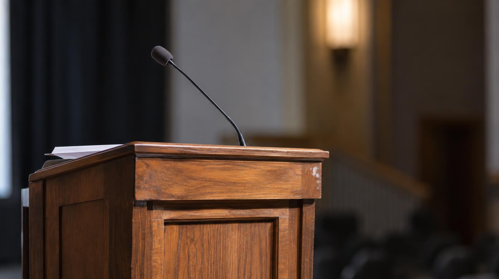 A wooden lectern with a microphone on a softly lit stage.