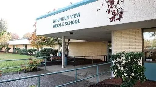 Exterior entrance of a single-story brick school building with covered walkway and green railing.