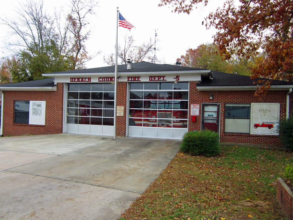 Small brick fire station with two white garage doors and an American flag on a flagpole.