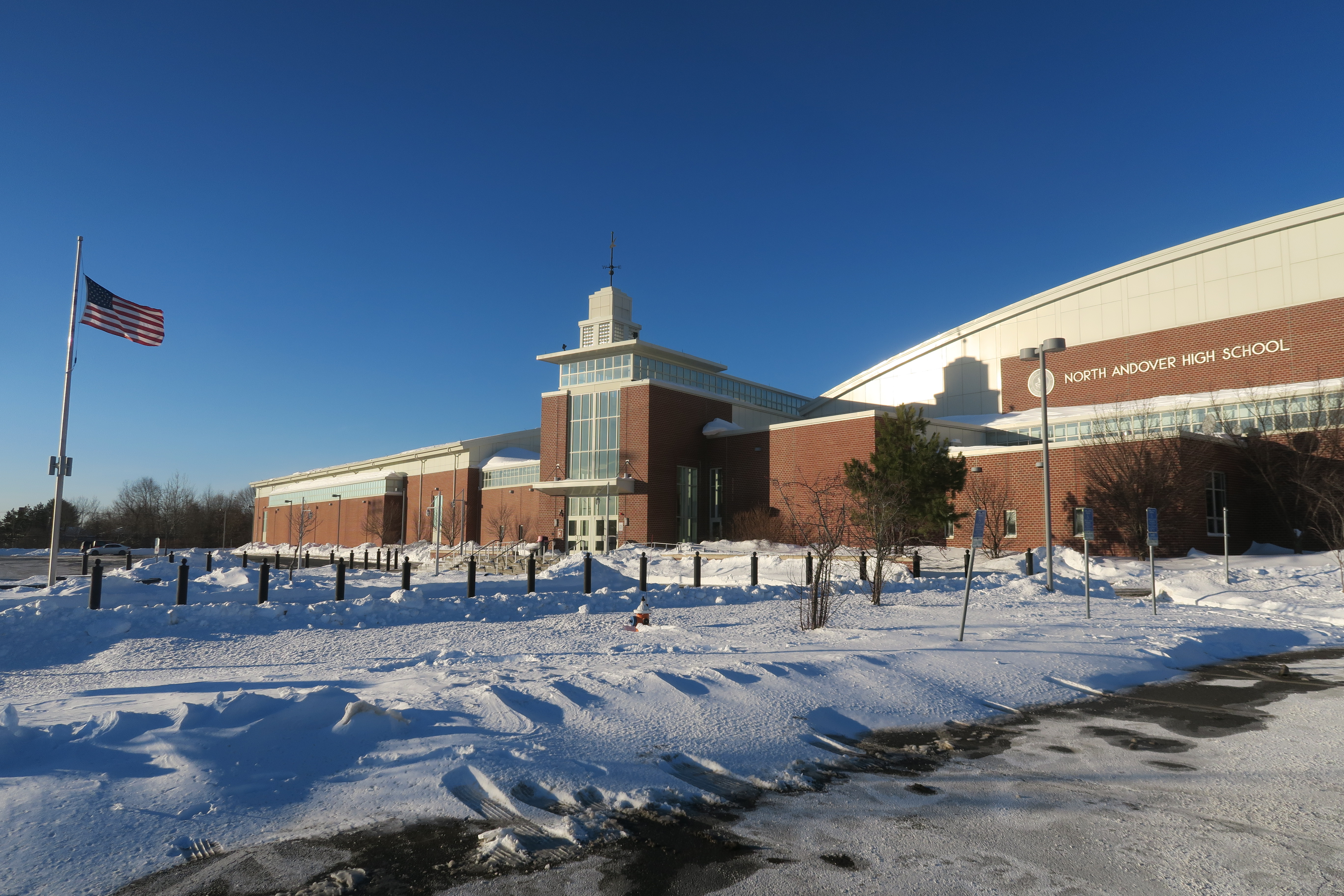 Red brick school building with flagpole and snow-covered grounds under blue sky.