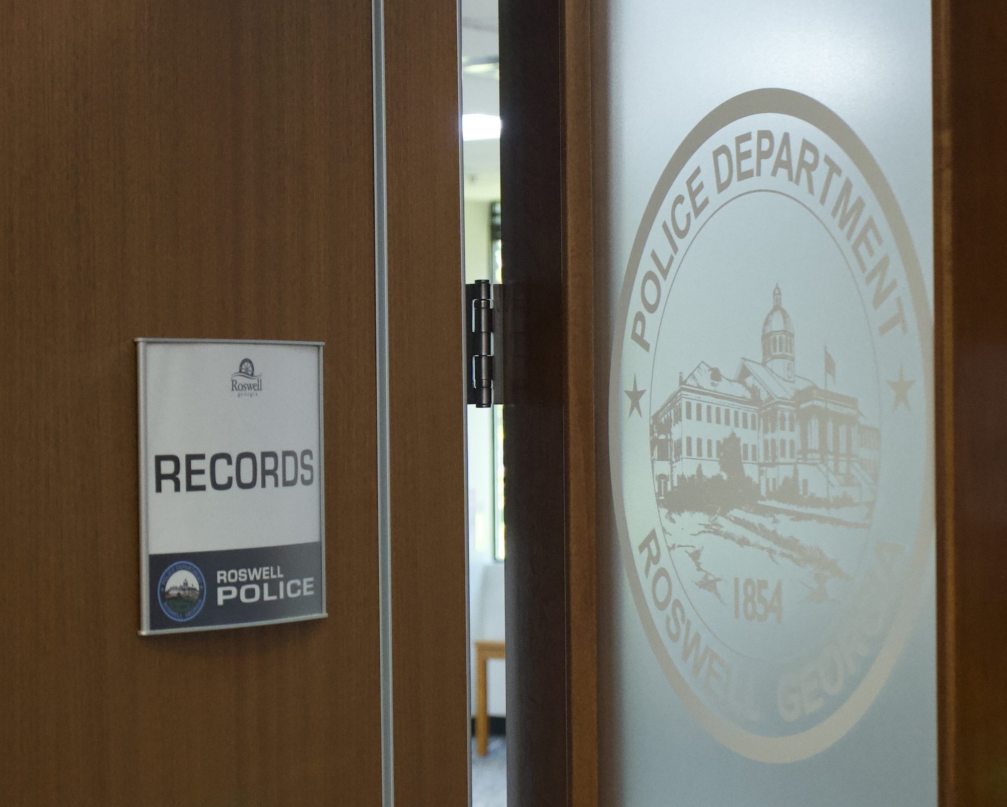 Records office door with a police department seal on frosted glass, standing ajar.