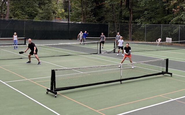 Several players playing pickleball on outdoor hard courts with a portable net.