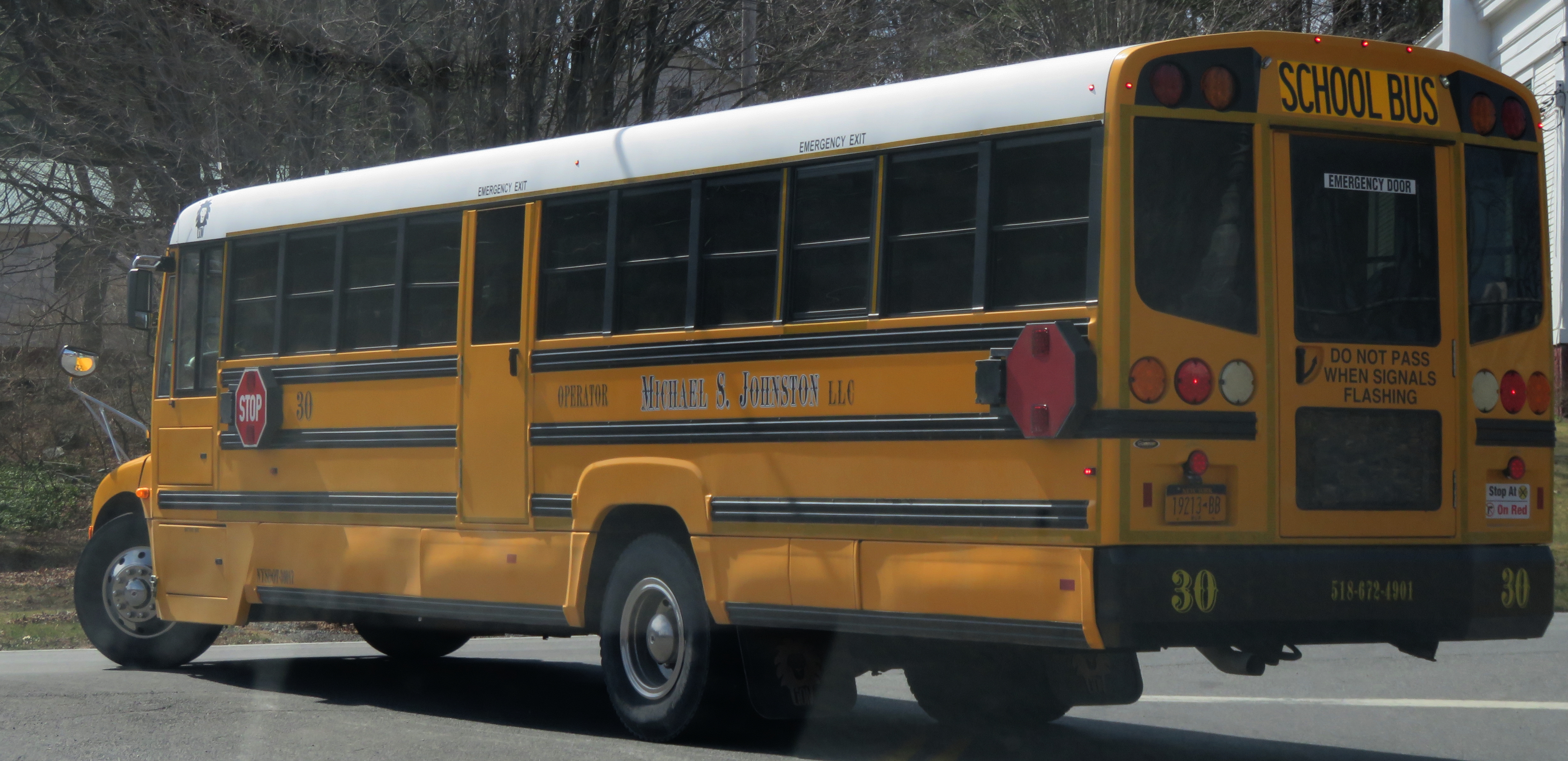 Yellow school bus viewed from the rear with stop arm and safety stripes visible.