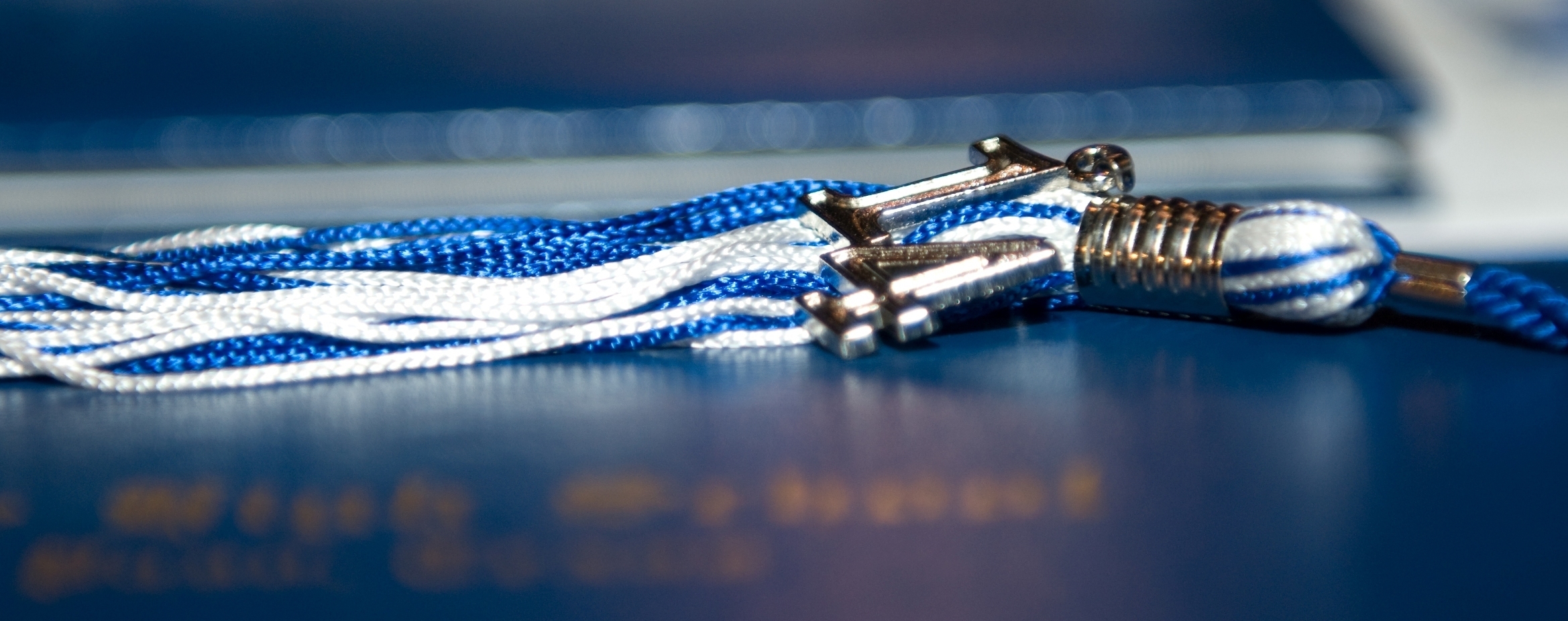 A blue and white graduation tassel resting on a dark navy diploma cover.