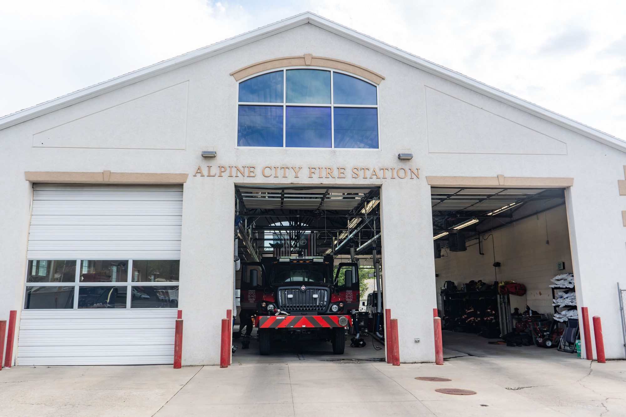 Fire station exterior with open bay doors and red fire truck inside.