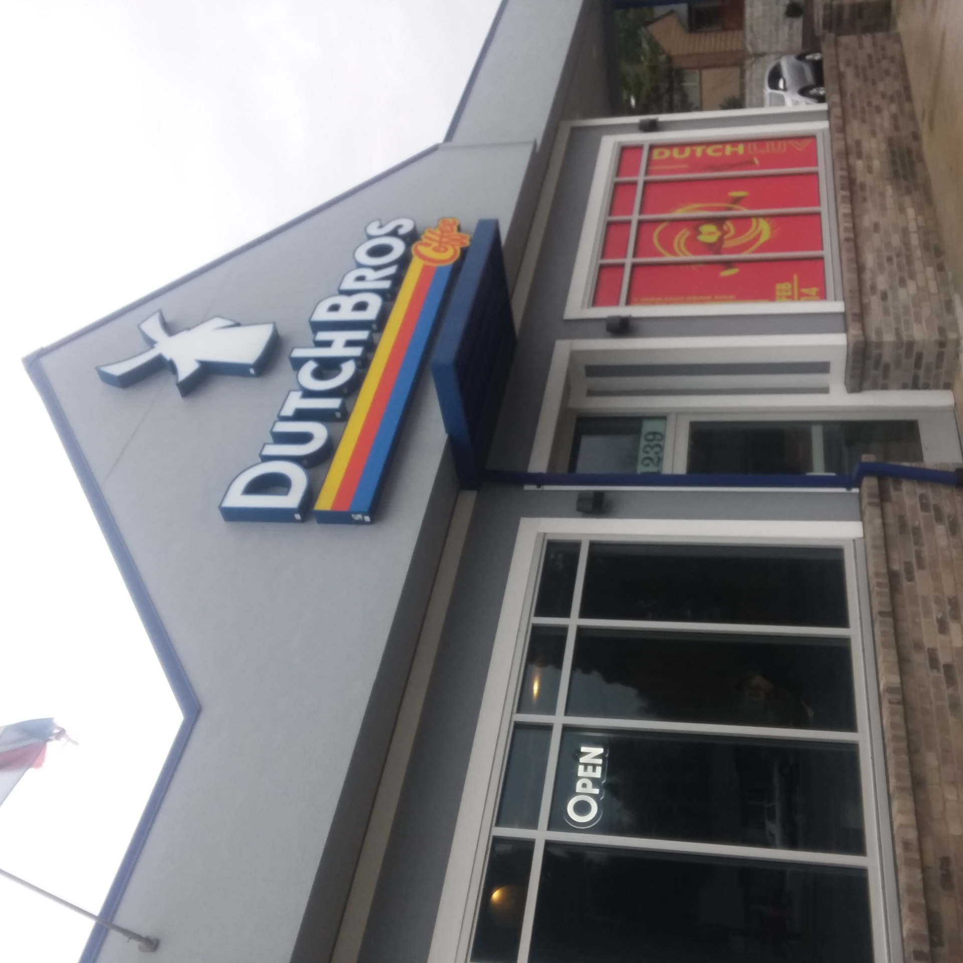 Gray building with blue awning and Dutch Bros Coffee windmill logo sign.