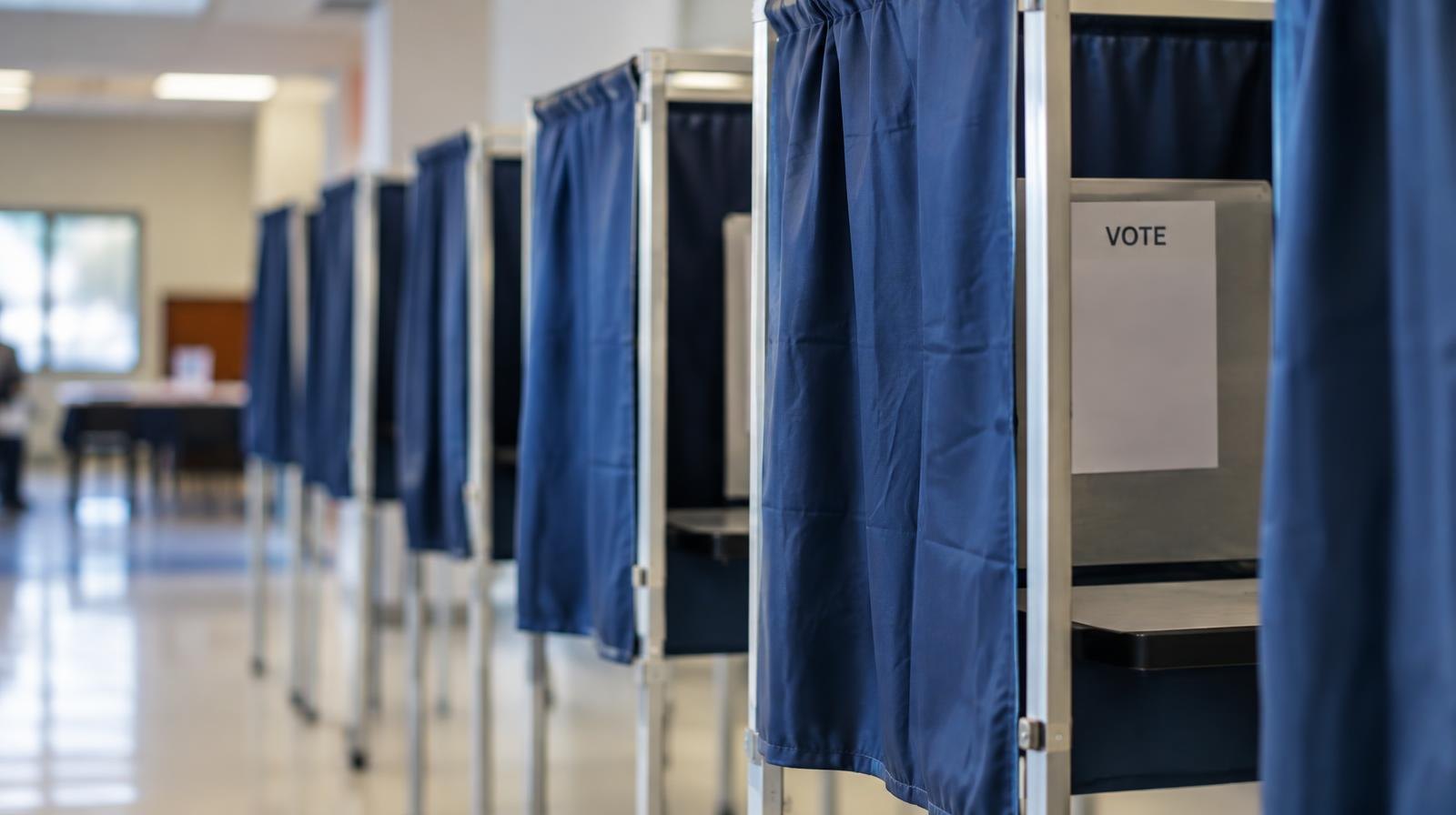 A row of empty voting booths with privacy curtains inside a polling place.