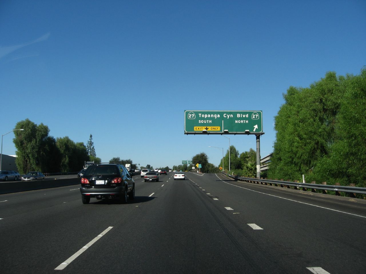 Overhead green freeway sign for Topanga Canyon Boulevard on a multi-lane highway with vehicles.