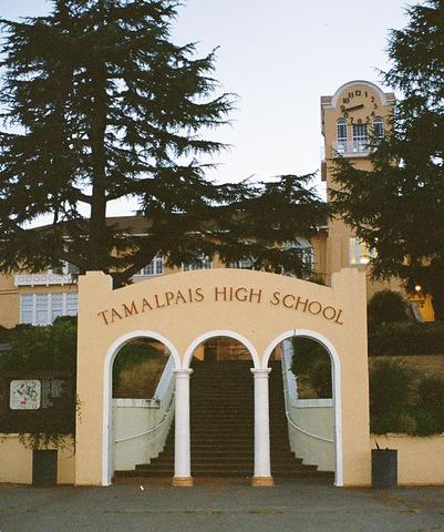 Stone arched entrance gate of a high school with a clock tower visible behind it at dusk.