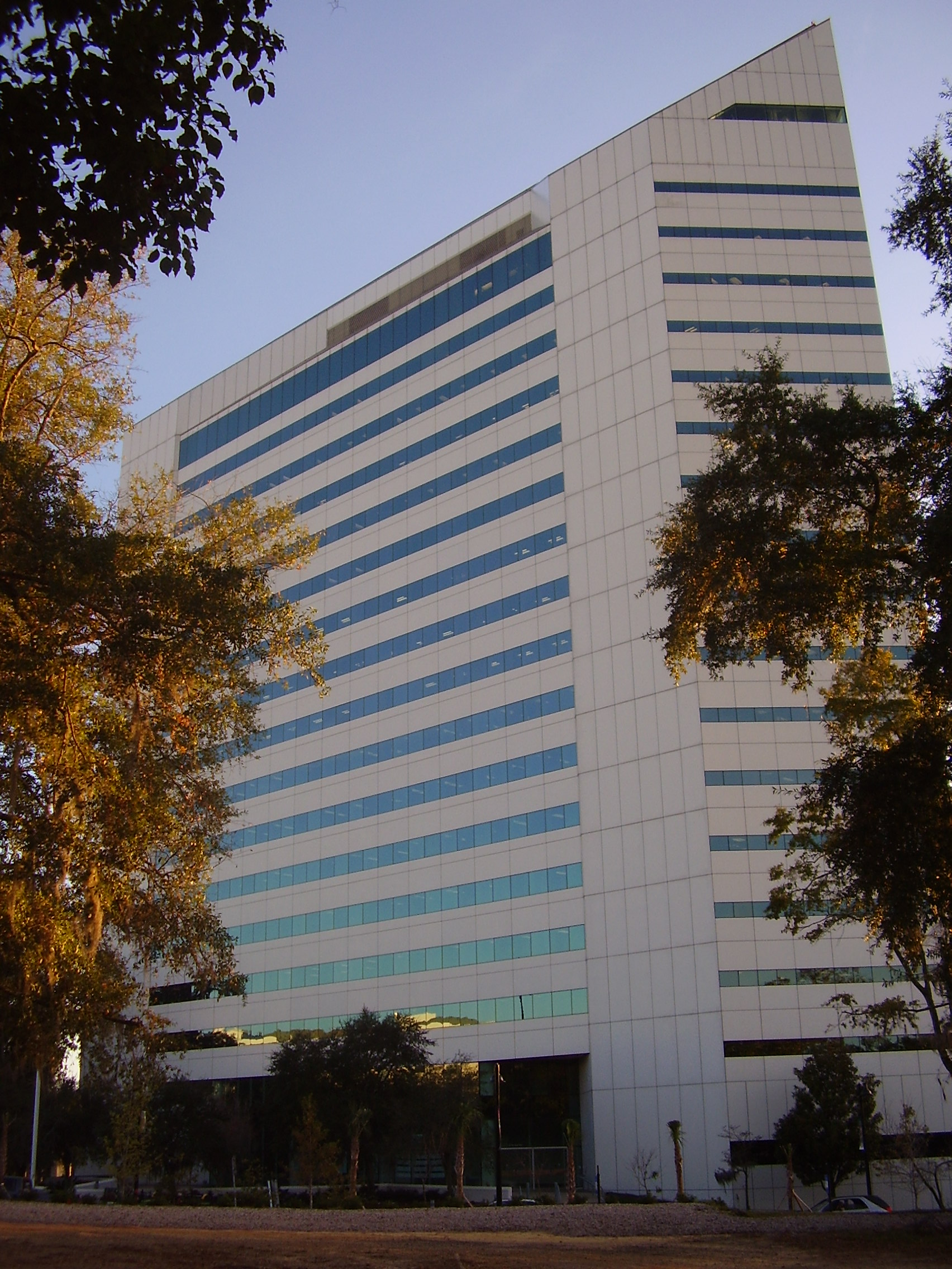 Tall white office building with tinted windows surrounded by trees.