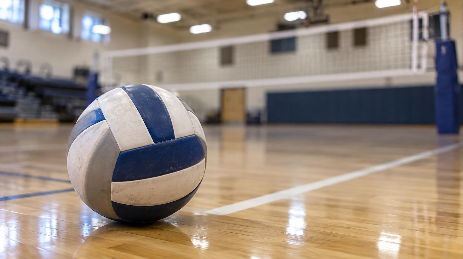 A volleyball resting on a hardwood gymnasium floor near a net.