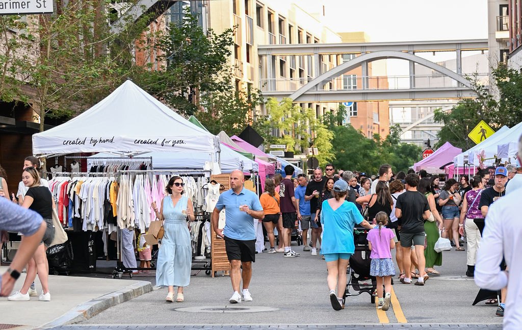 Crowds walk past vendor tents lining a closed urban street at an outdoor market.