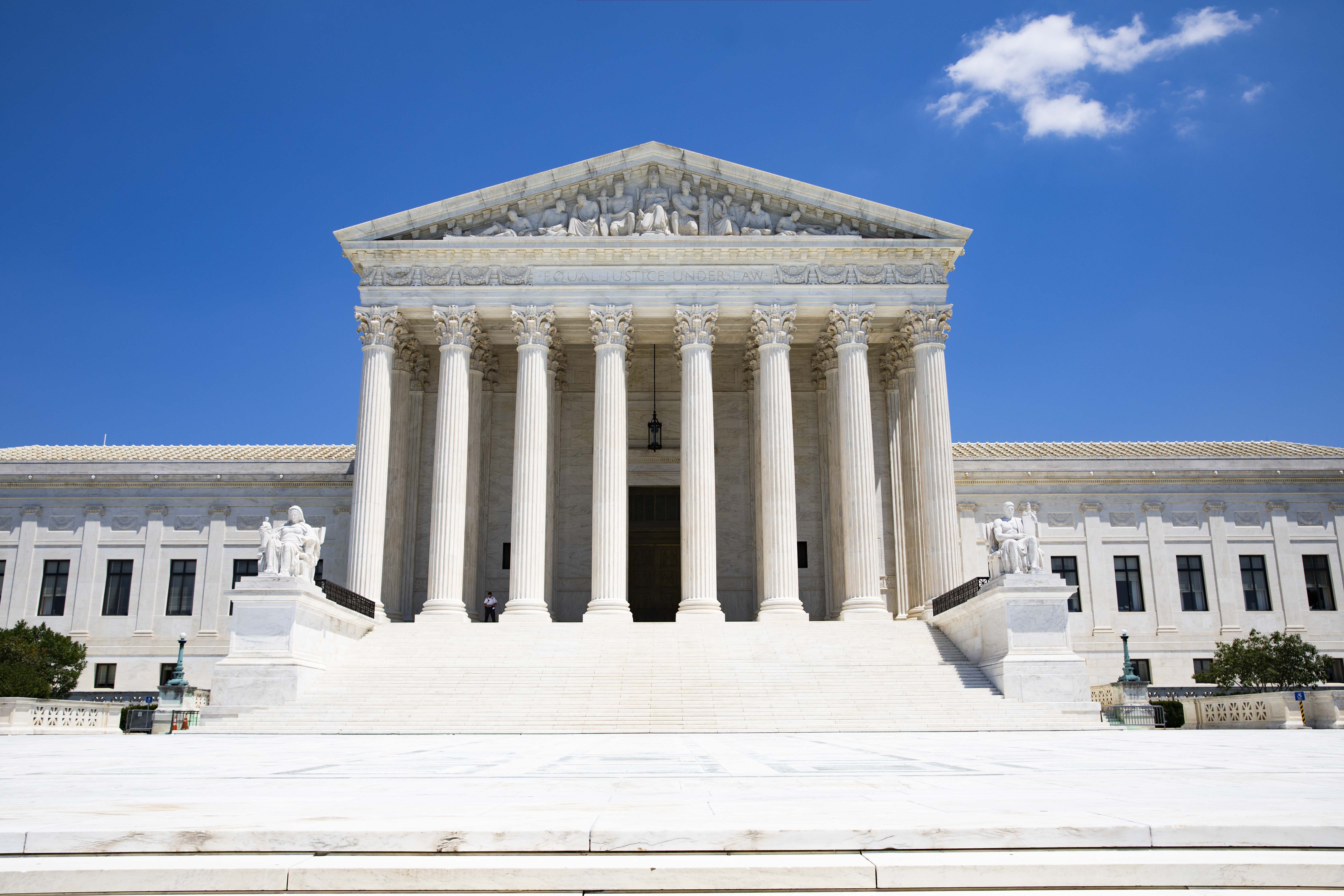 White marble Supreme Court building with tall columns and broad steps under a blue sky.