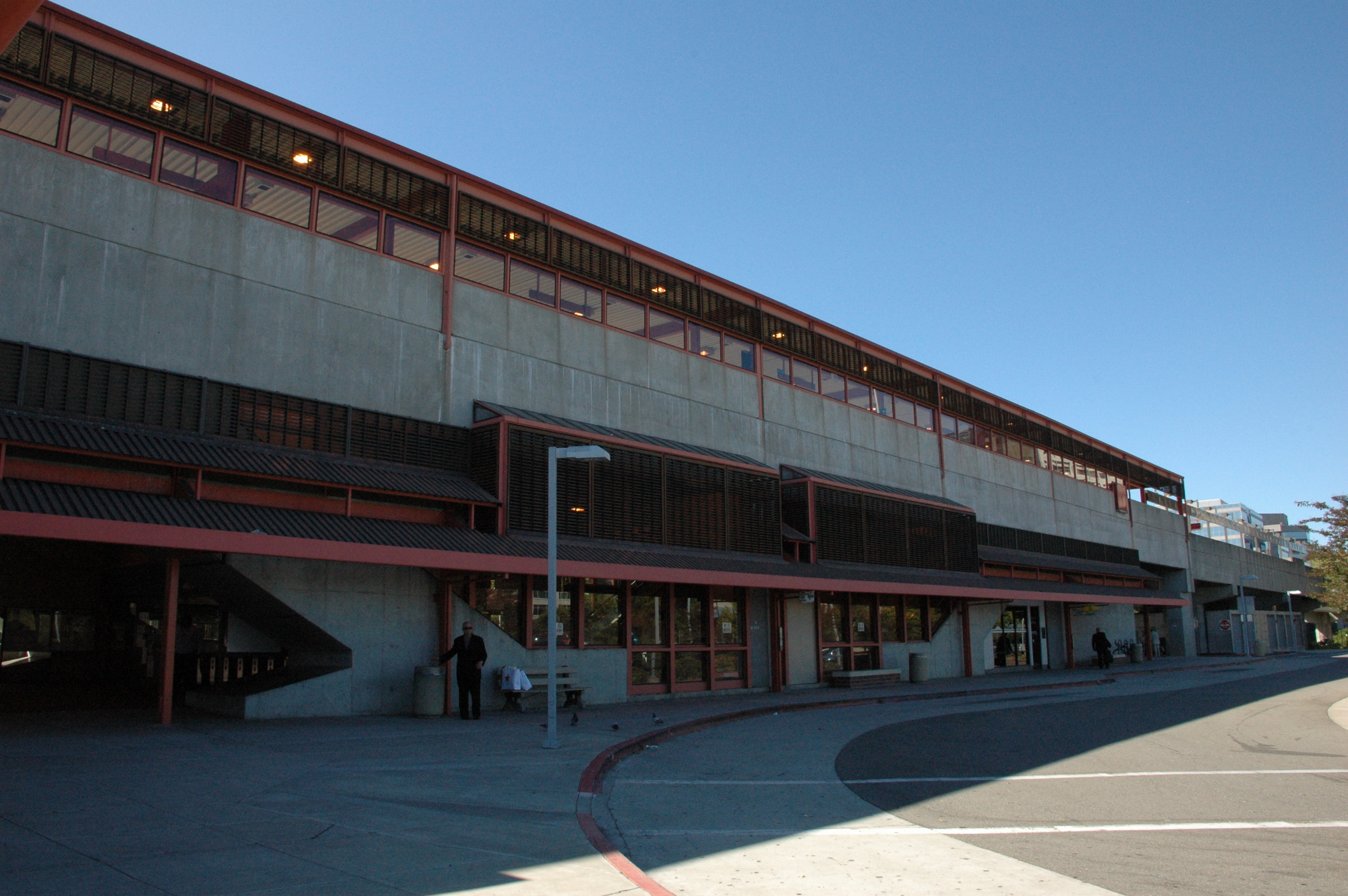 A multi-story concrete transit station building with red trim and a covered walkway.