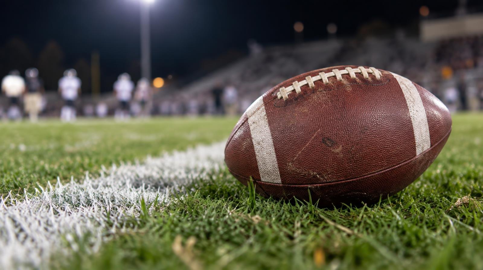An American football resting on green grass next to a white yard line.