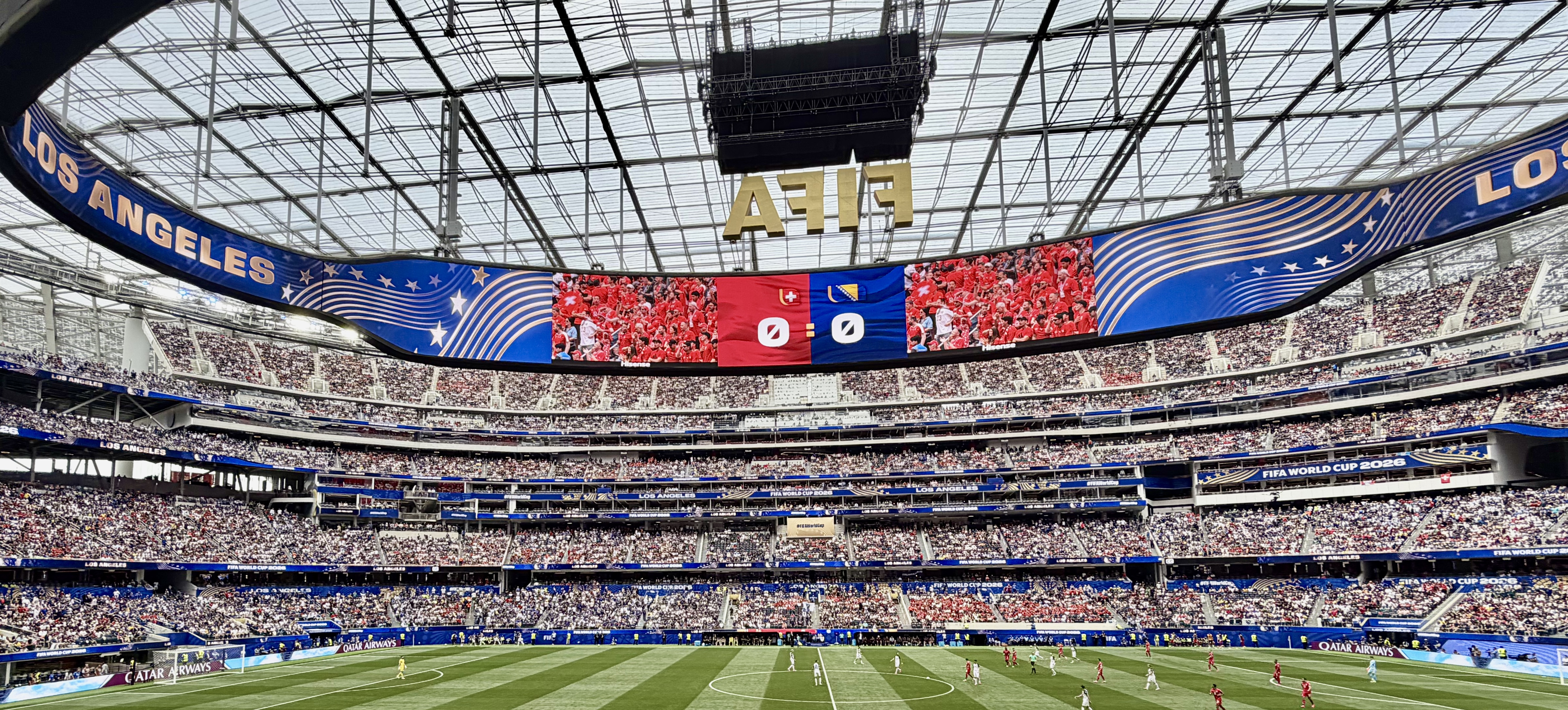 Panoramic interior view of a packed stadium during a FIFA World Cup match with FIFA branding on the scoreboard.