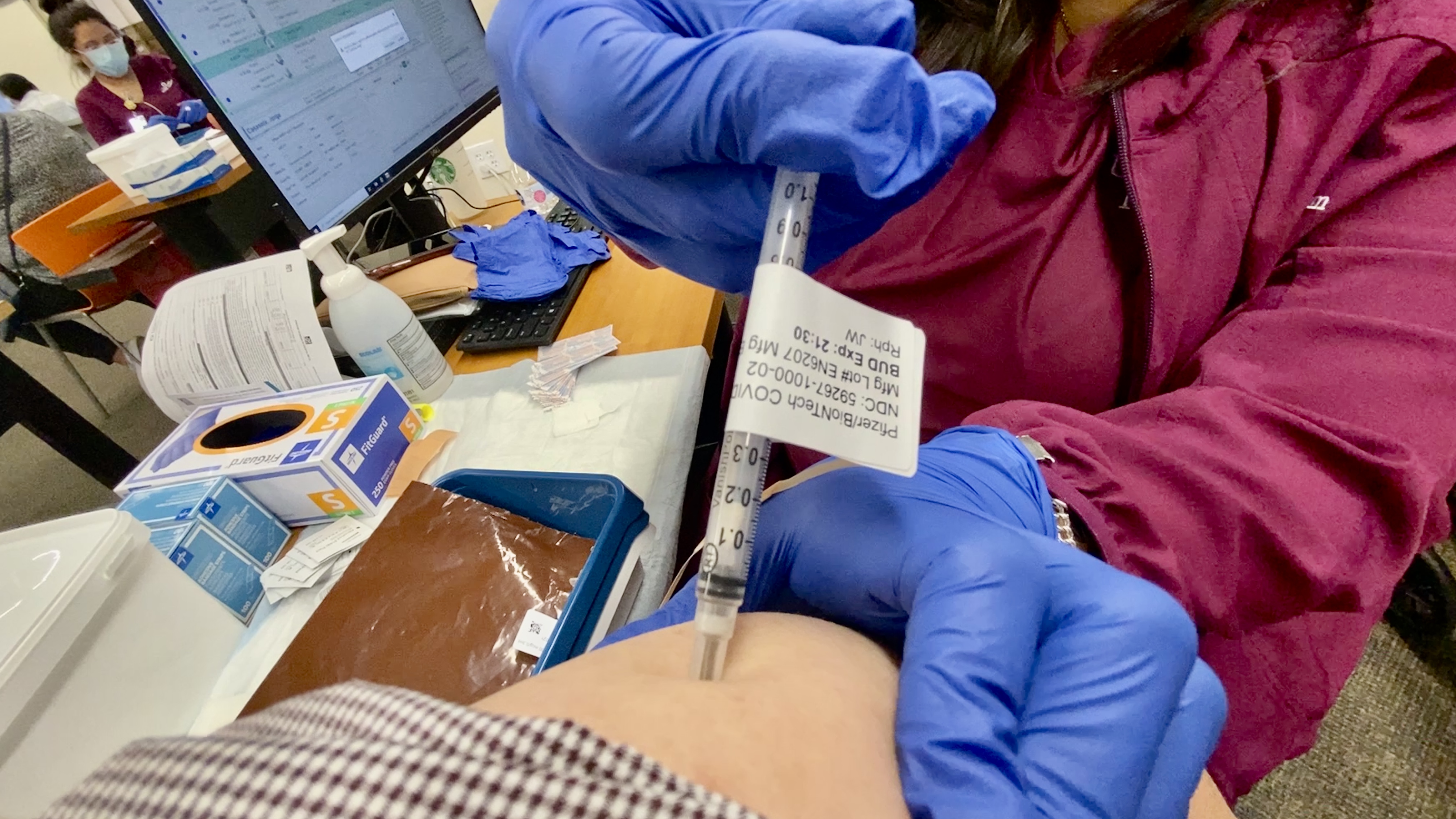 Gloved healthcare worker injecting a vaccine into a patient's upper arm at a clinic.