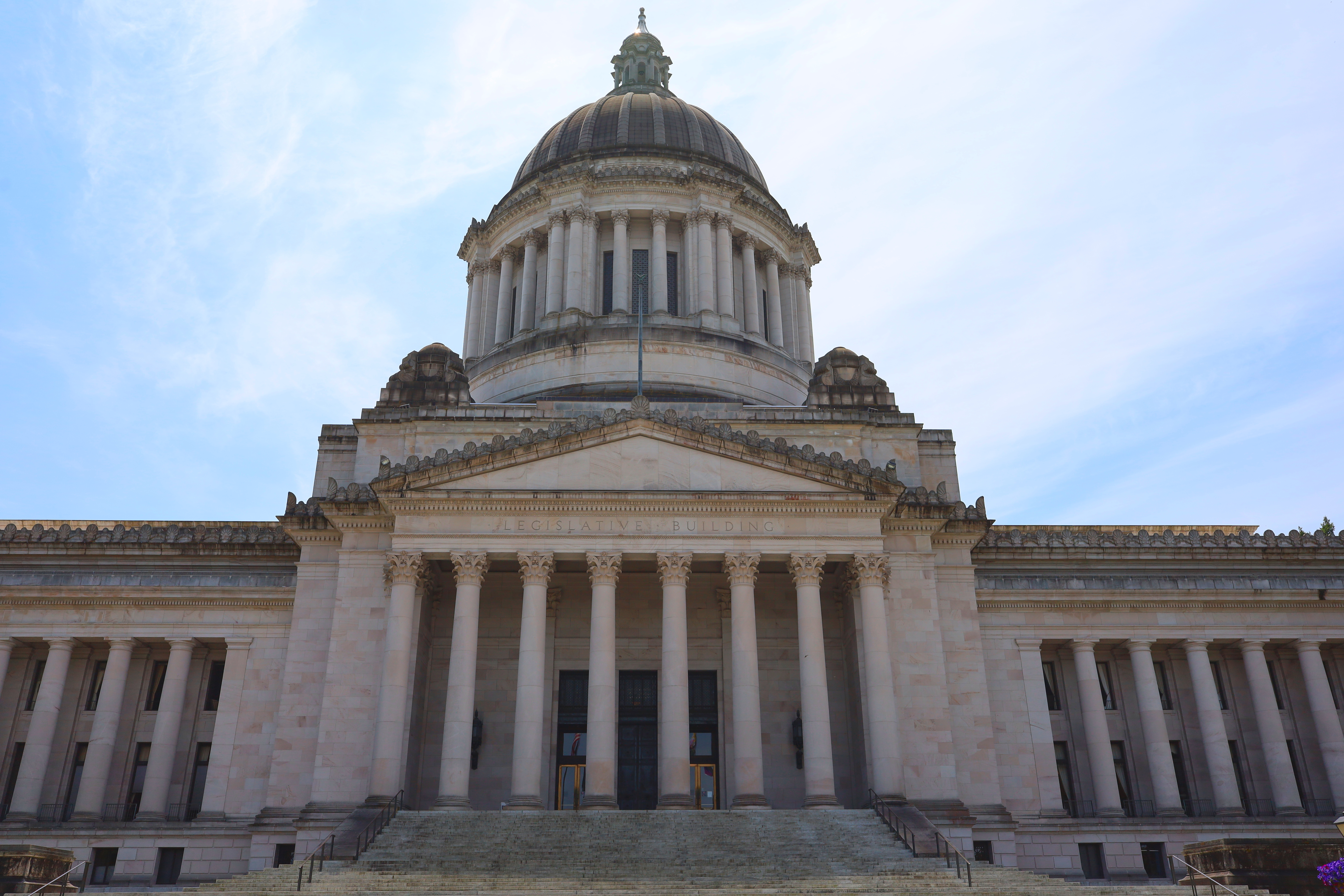 Grand stone steps leading up to a neoclassical domed capitol building under a partly cloudy sky.