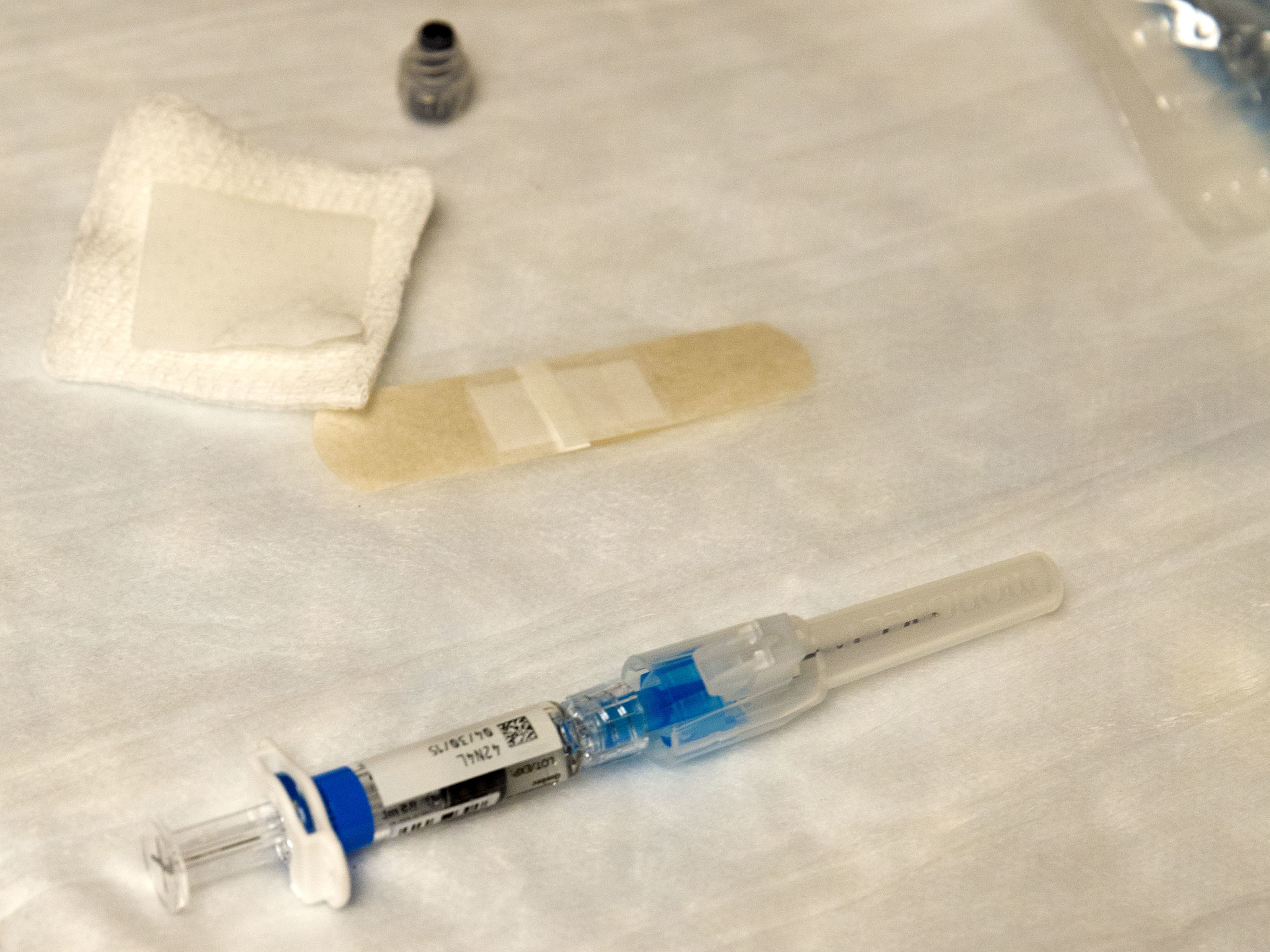 A pre-filled flu vaccine syringe with a blue plunger beside a bandage and gauze on a white surface.