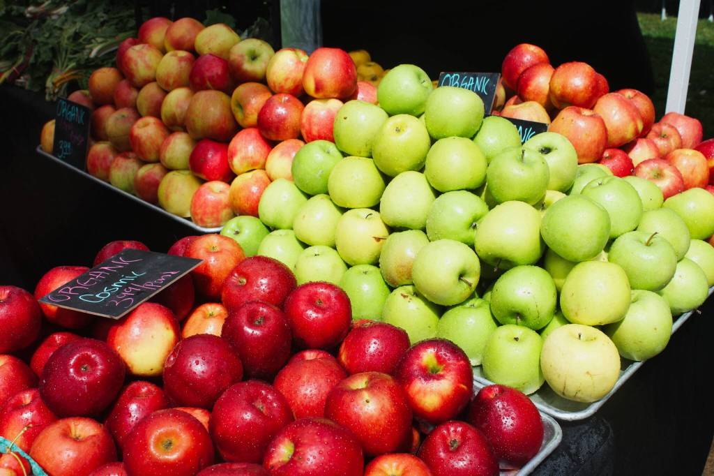 Bins of red and green apples displayed for sale at an outdoor farmers market.