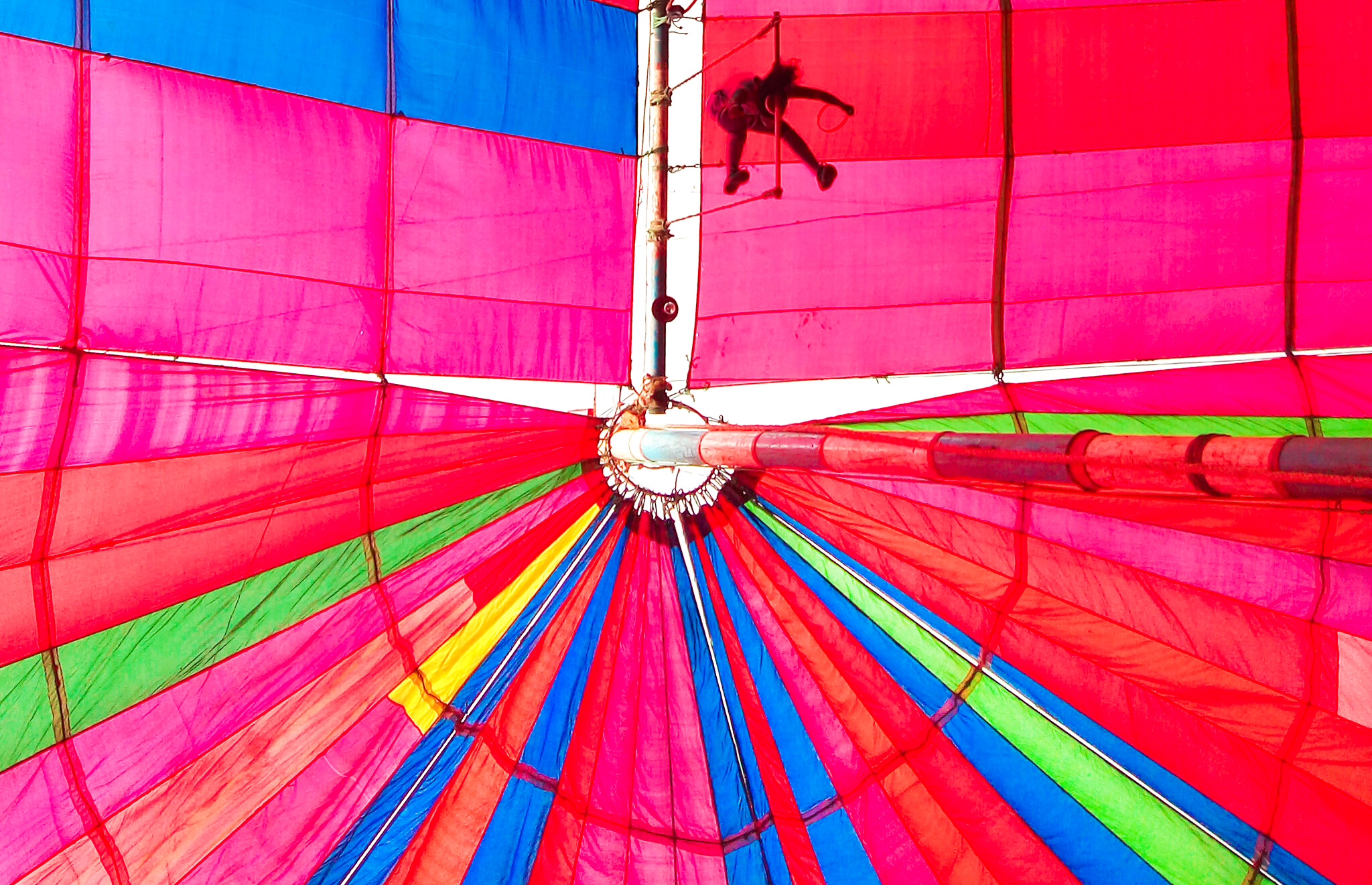Silhouette of a performer suspended near the top of a vibrant striped circus tent.